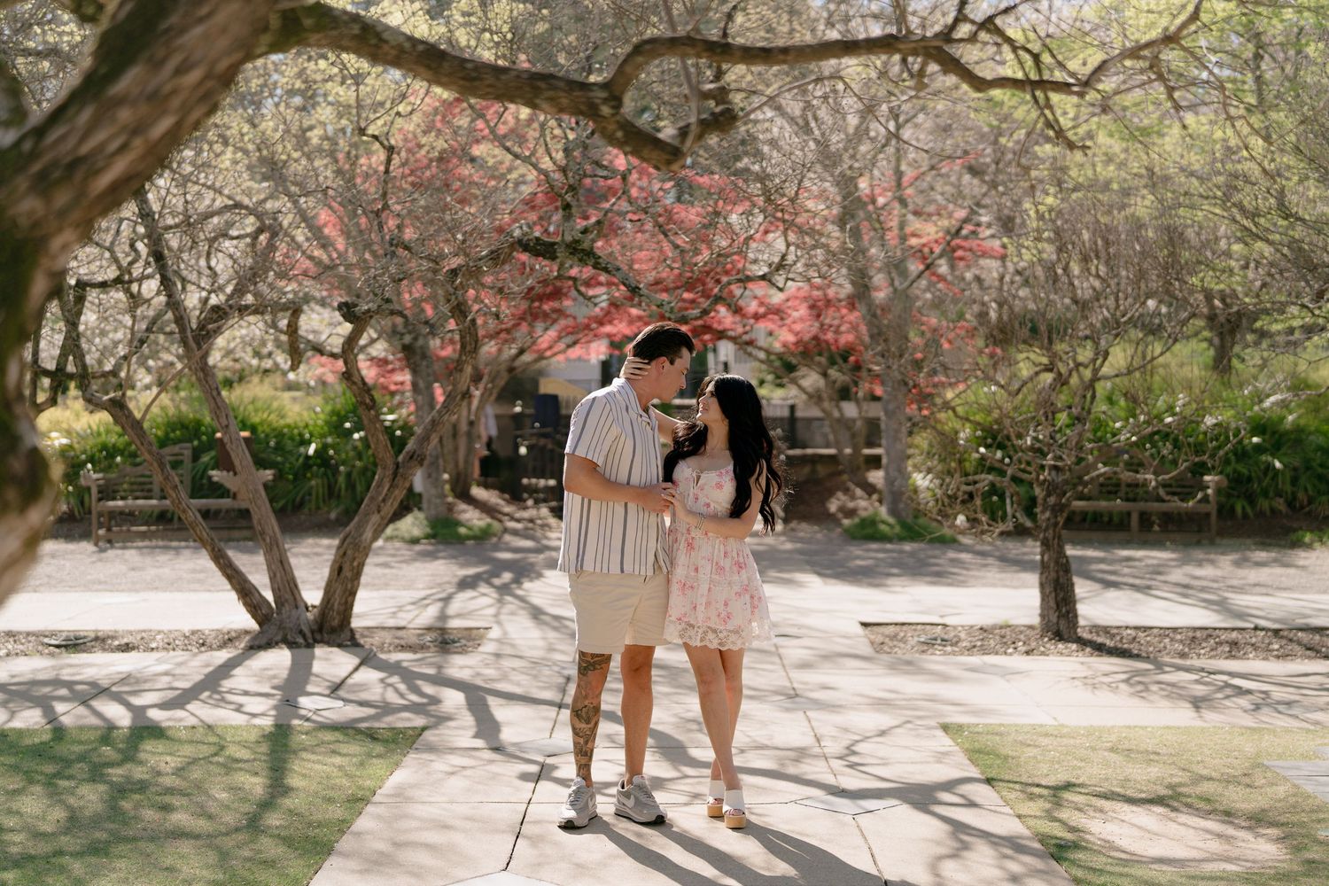 Couple sharing a romantic moment on a garden path surrounded by blooming spring trees in soft natural light.