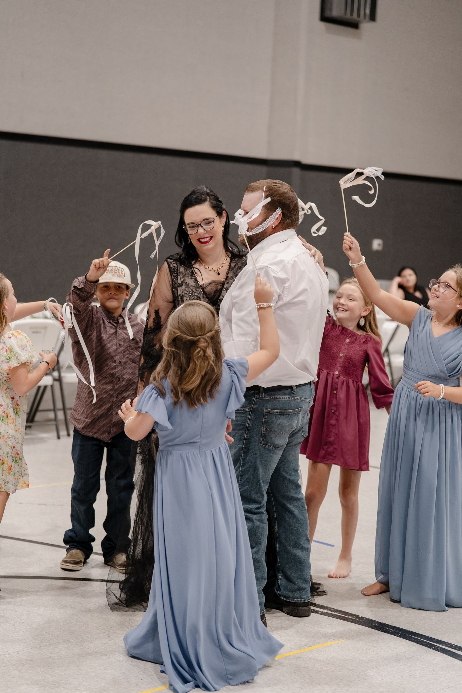 Wedding party celebrates with dancing and laughter in a reception hall with guests wearing blue dresses.