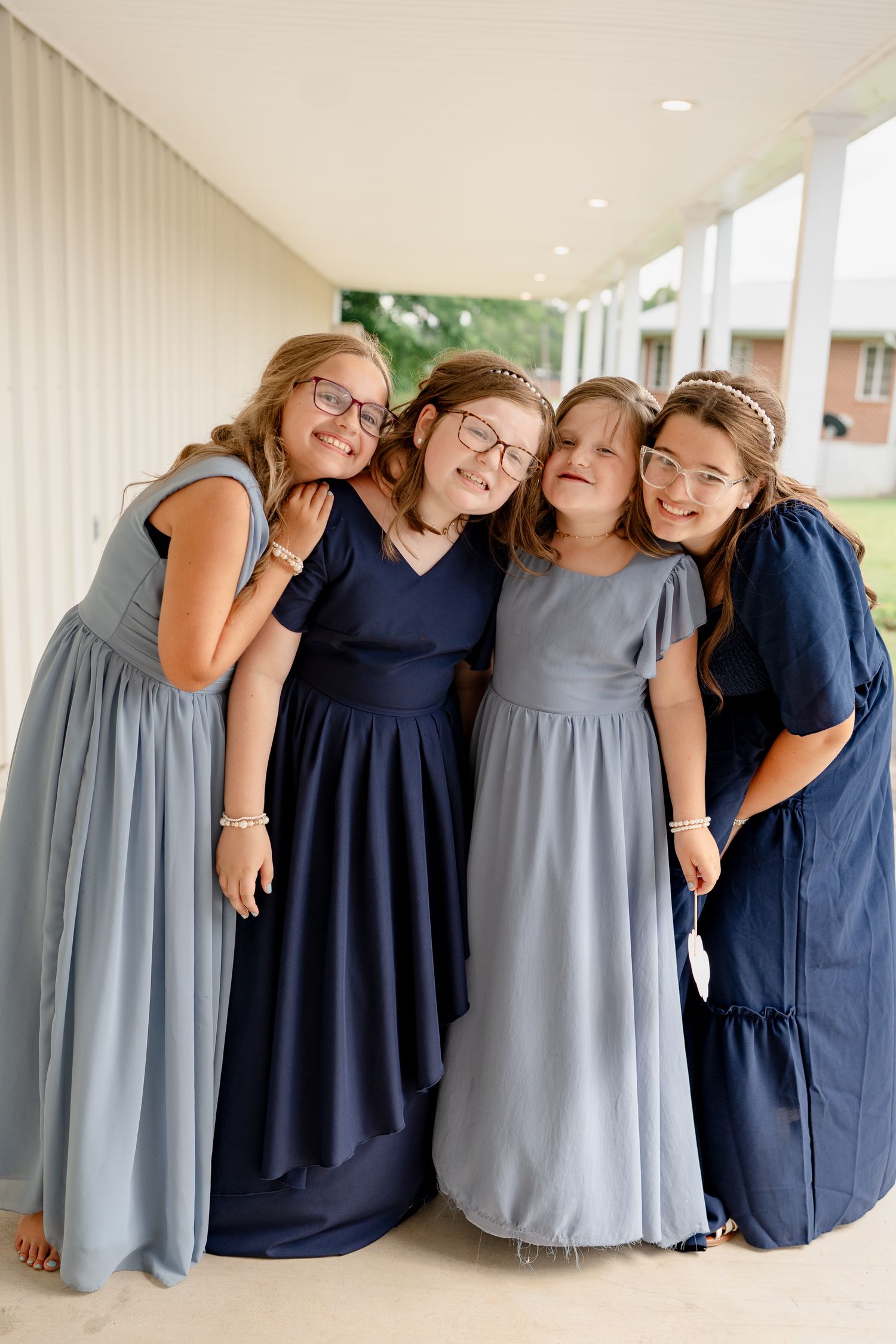 A group wearing coordinated navy blue and gray dresses poses together on a covered walkway.
