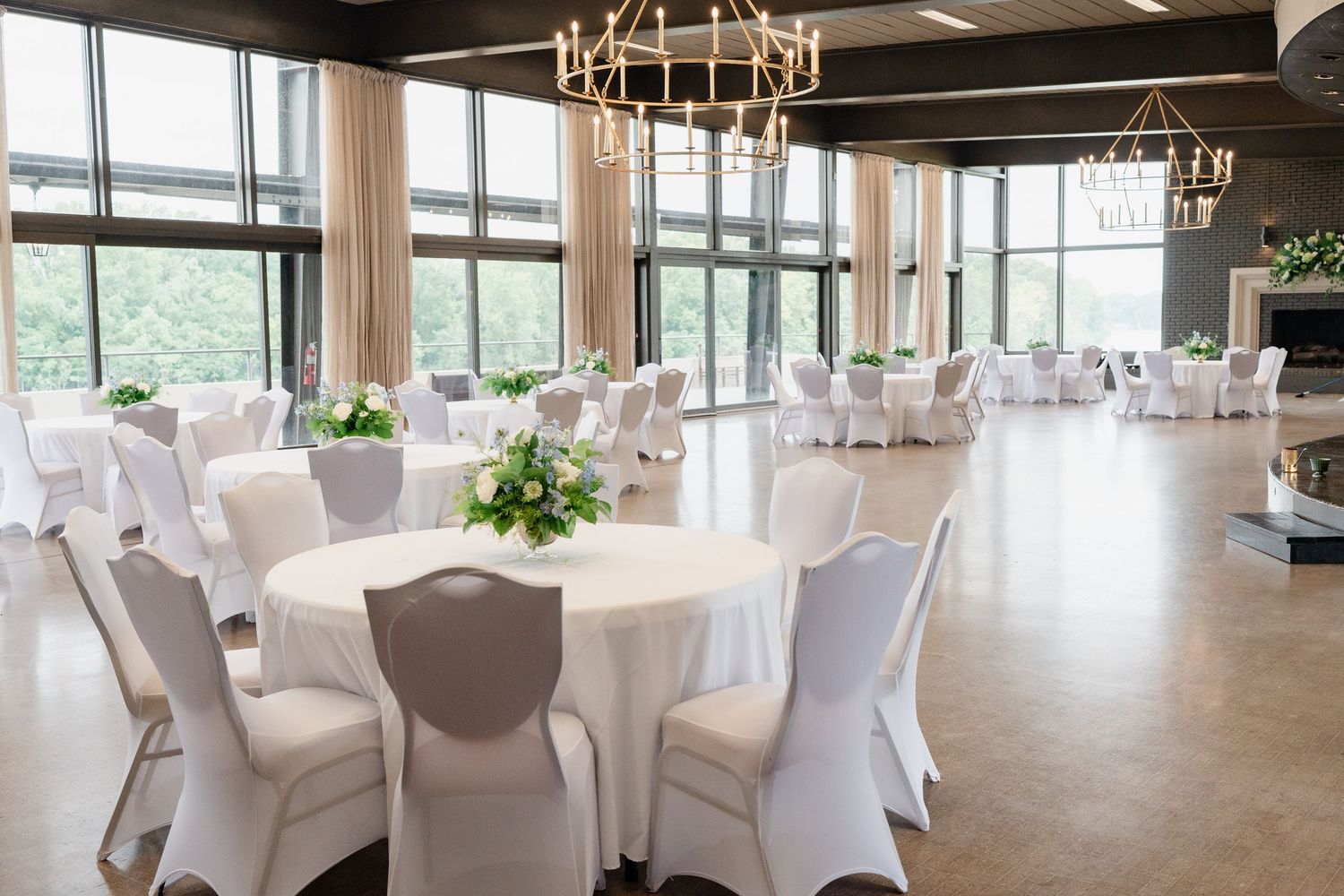 Elegant banquet hall with white chair covers, chandeliers, and floor-to-ceiling windows overlooking a scenic view.