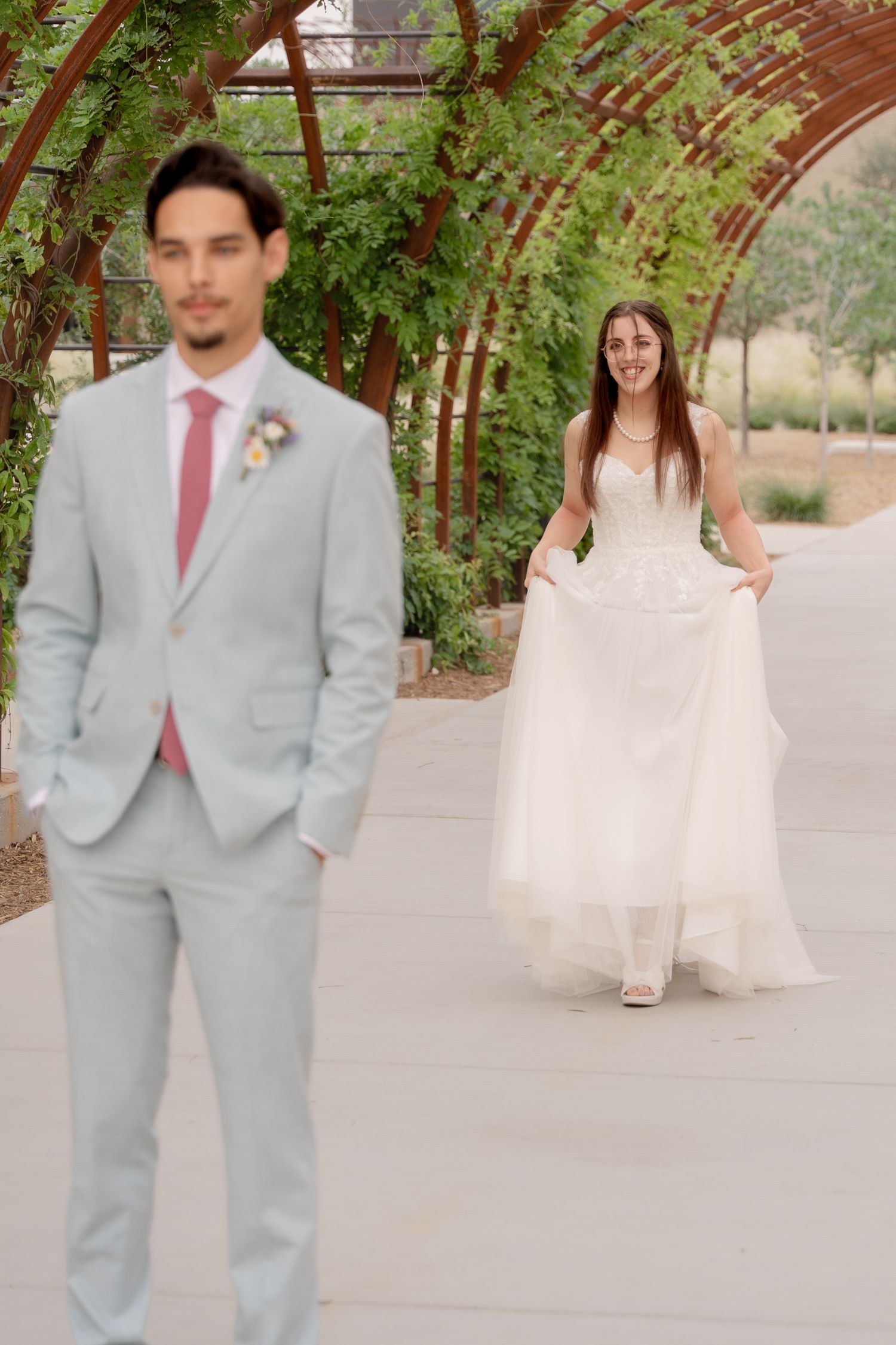 A romantic first look sequence between newlyweds under a wooden pergola with lush greenery.