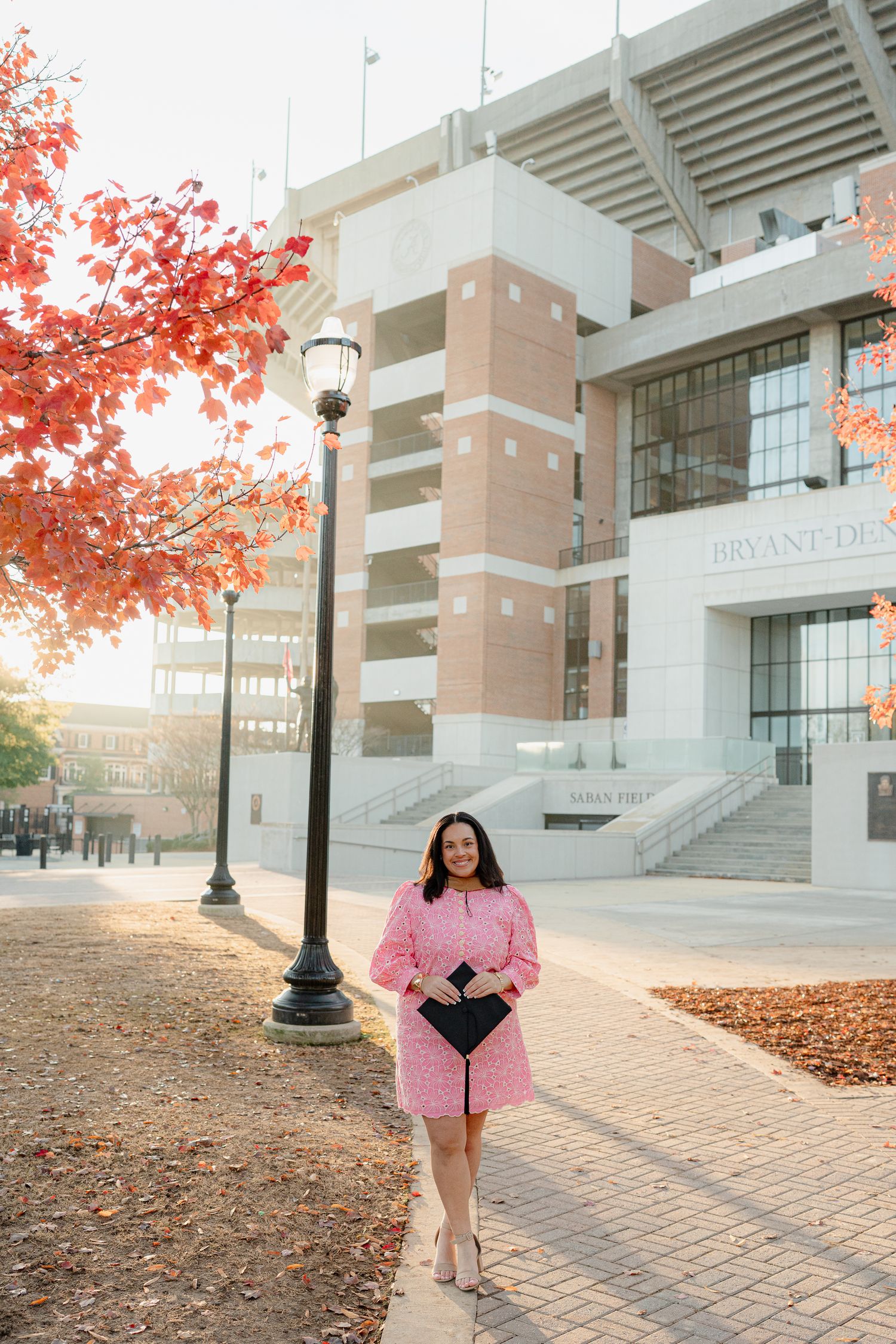A brick university building with autumn leaves and lampposts along a paved walkway during golden hour lighting.