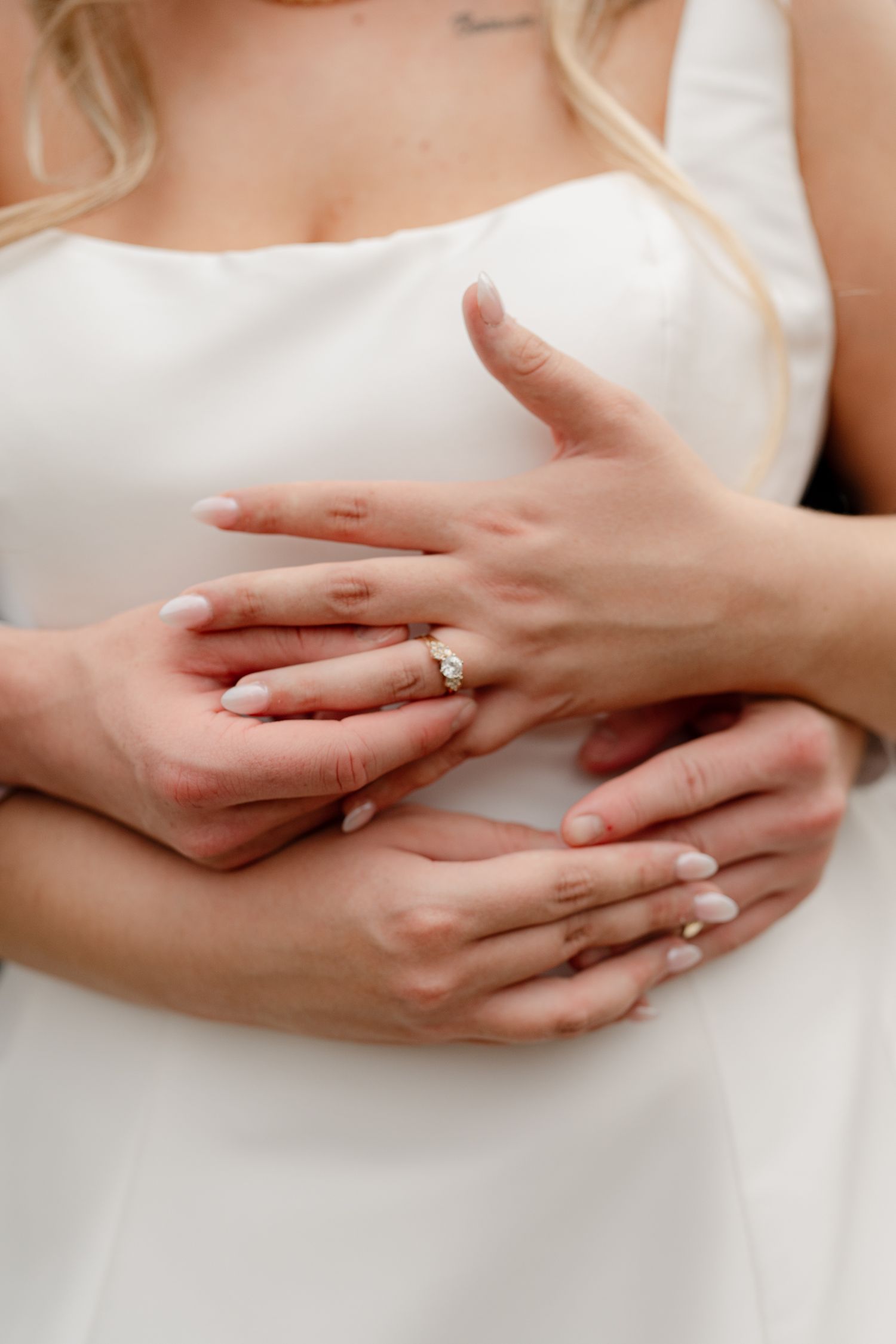 Close up view of hands with a wedding ring gently touching against a white fabric background.