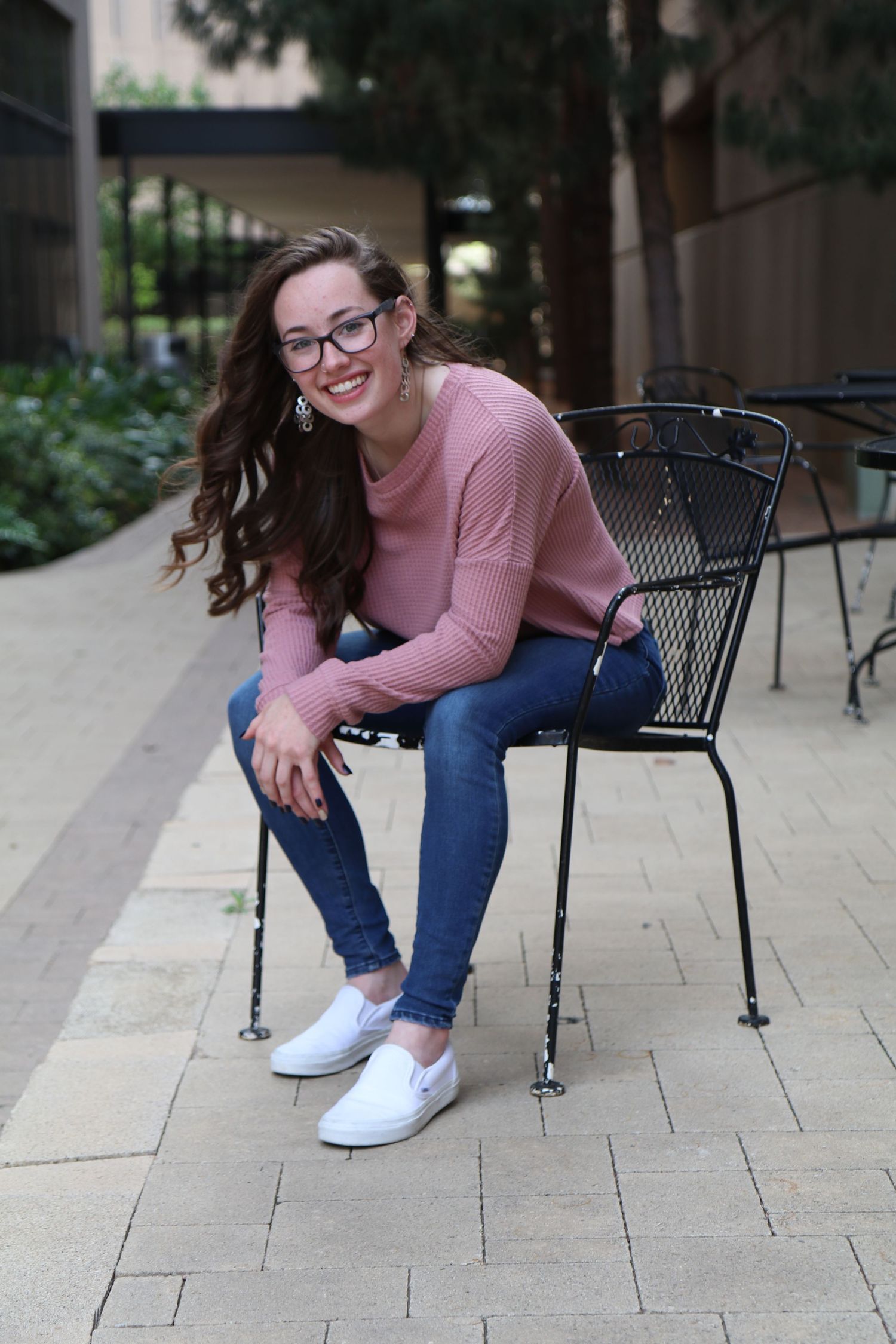 Casual portrait of woman in pink sweater sitting on metal chair outdoors.