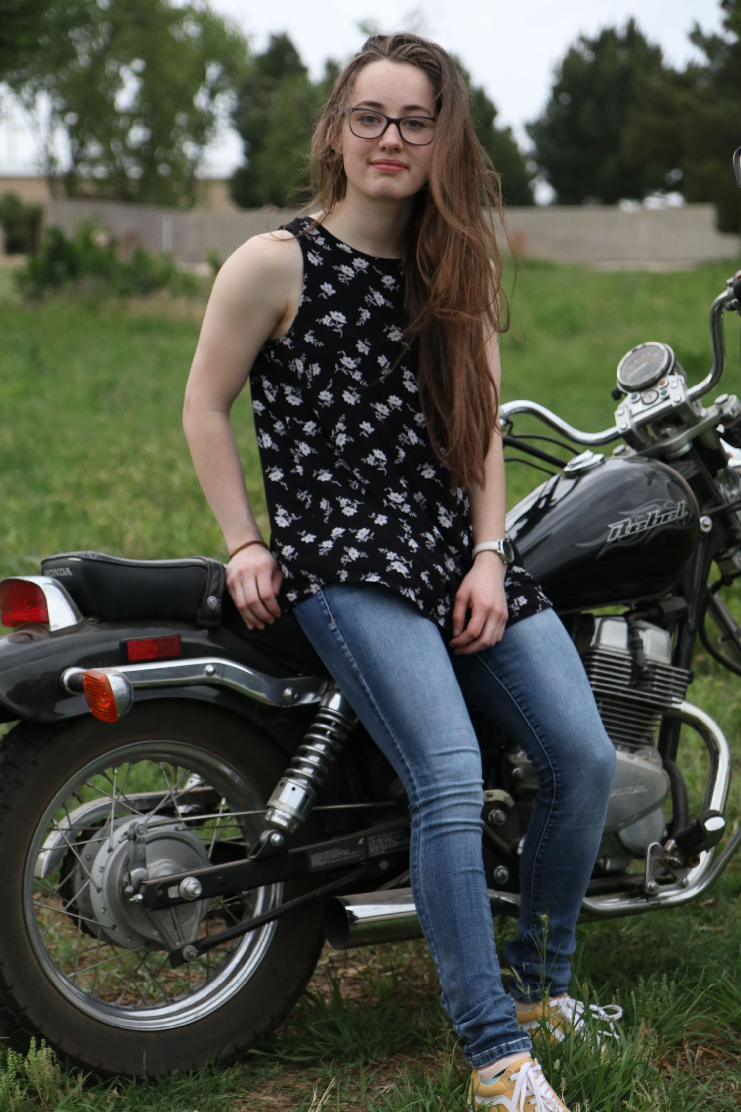 A vintage motorcycle enthusiast poses with a classic bike in a casual outdoor setting.