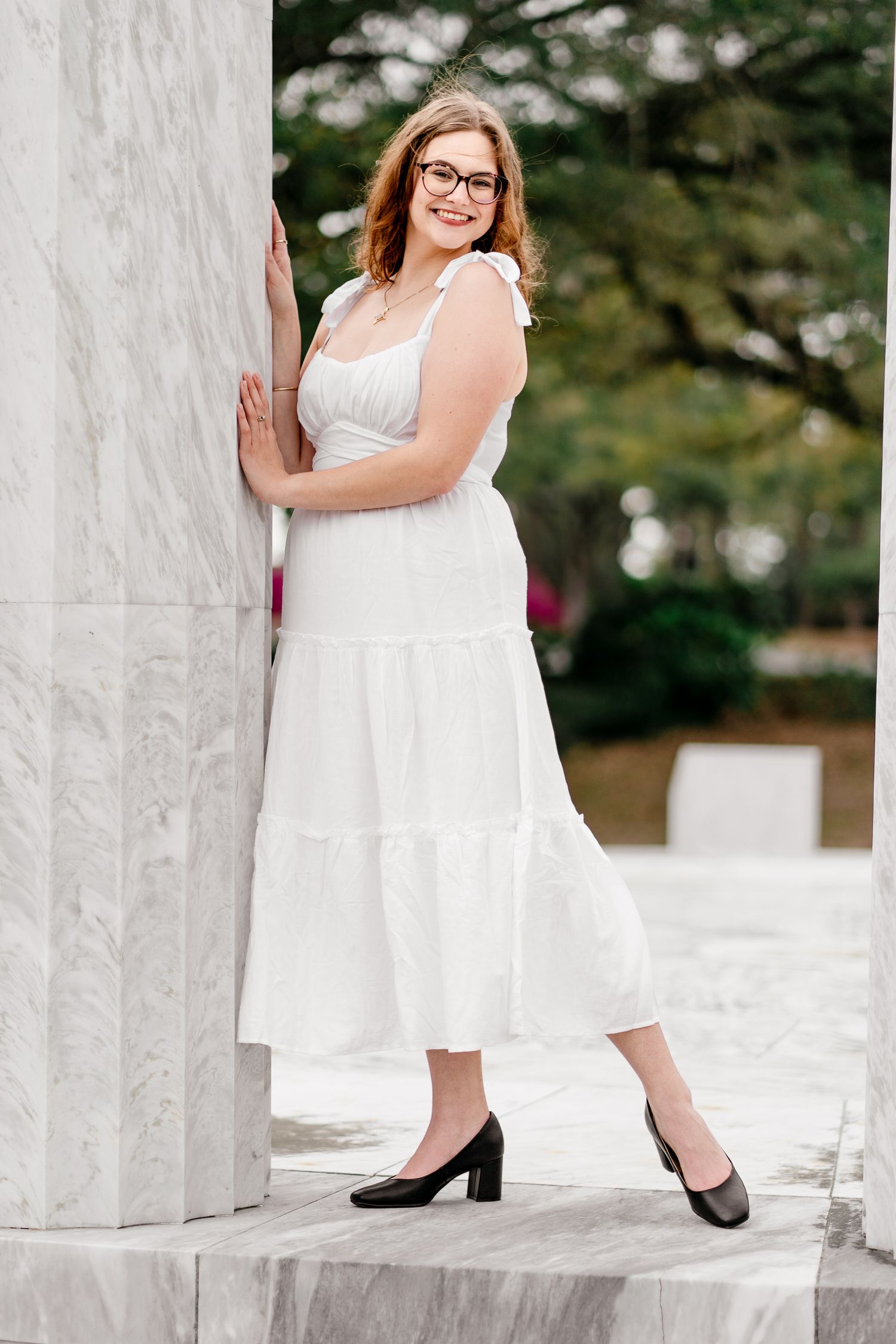 Graduate in white dress poses gracefully between white marble columns.