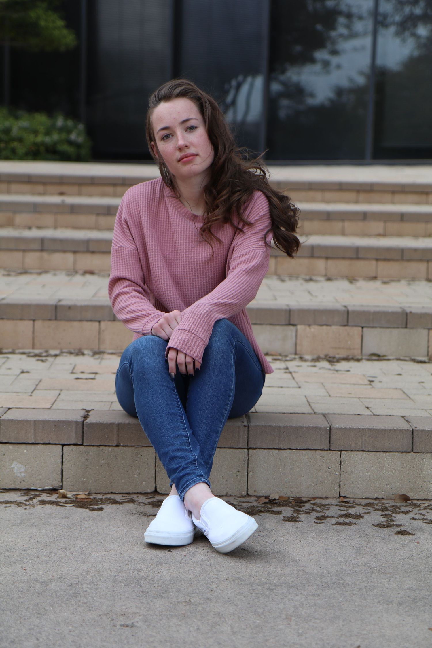Casual portrait on concrete steps wearing pink sweater and white sneakers.