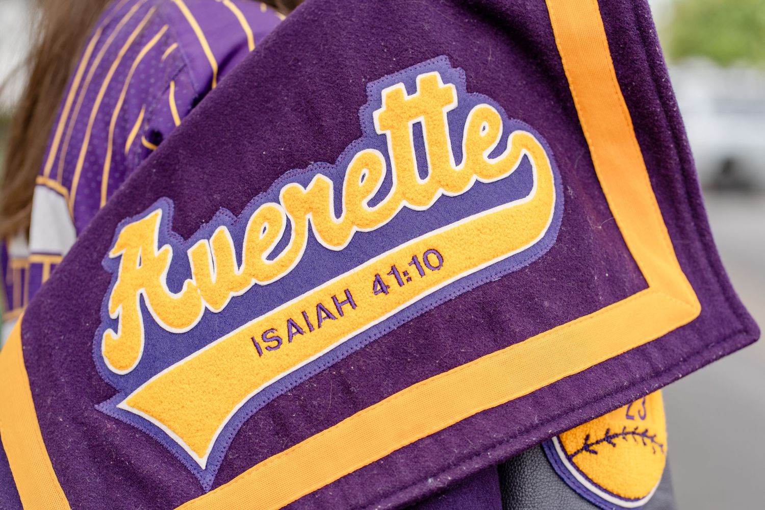 Purple and gold varsity letterman jacket with embroidered details shown in detail.
