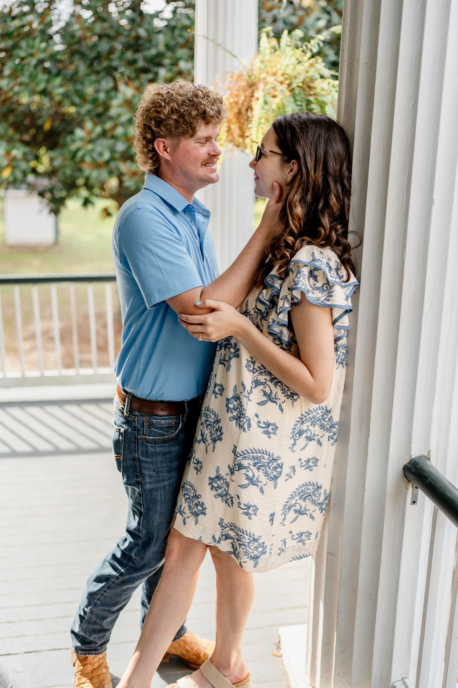 A couple embraces between white columns during an outdoor photoshoot.