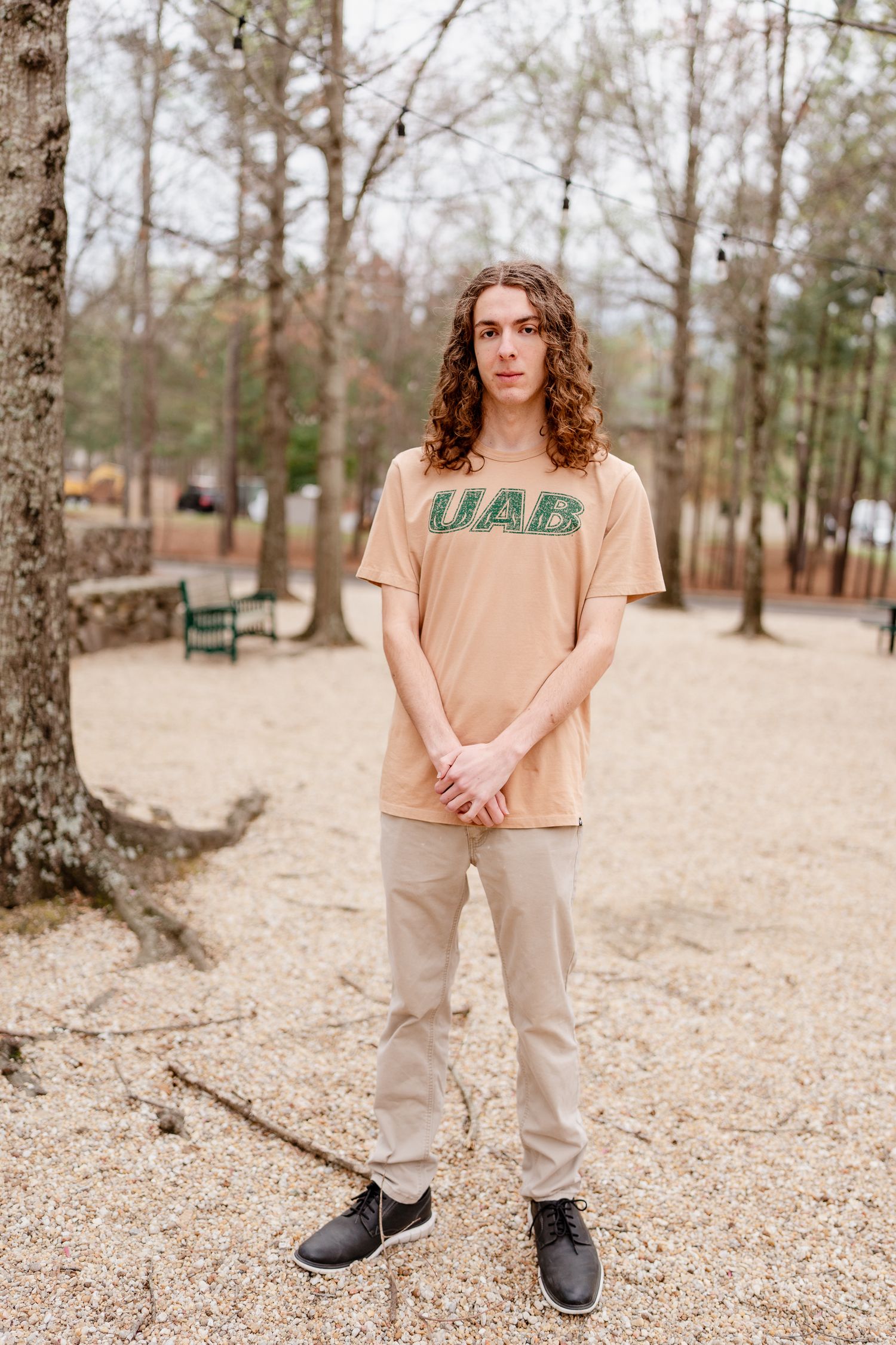 Person wearing UAB shirt standing in wooded outdoor area with stone walls.