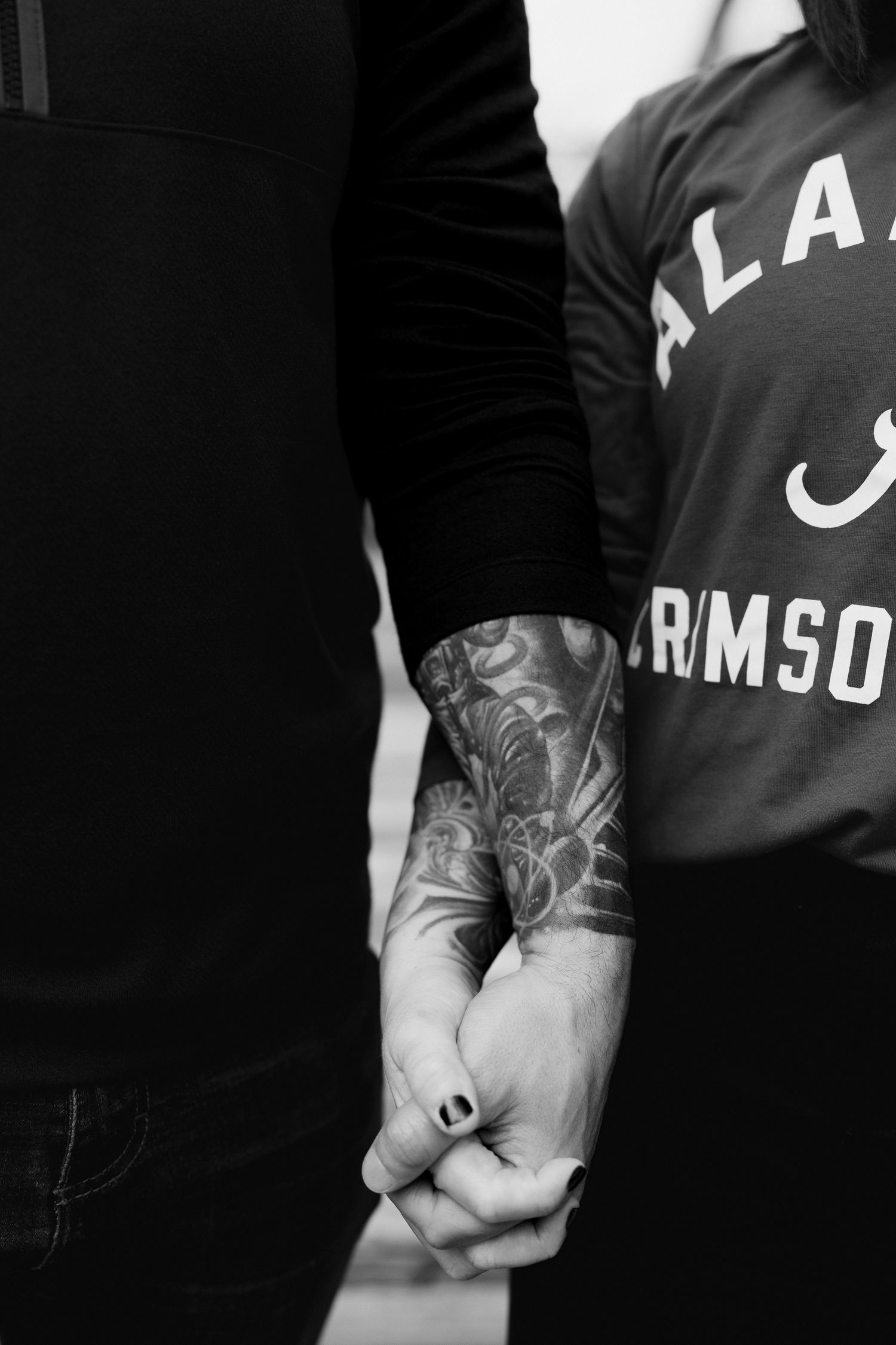 Close-up of intertwined hands with visible tattoo sleeve and Alabama Crimson text on clothing.