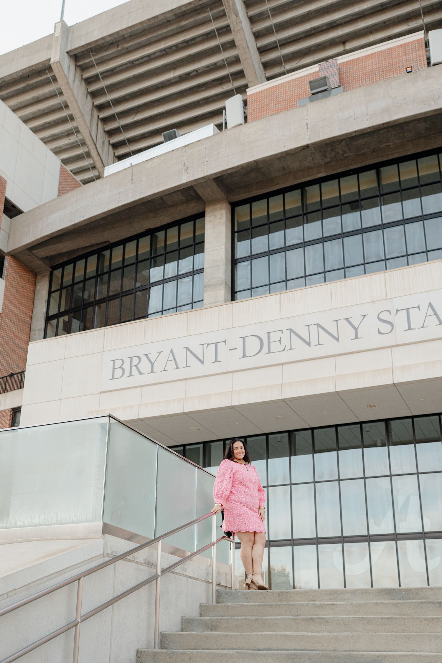 Person in pink outfit climbing stairs outside modern stadium building with glass windows and concrete architecture.