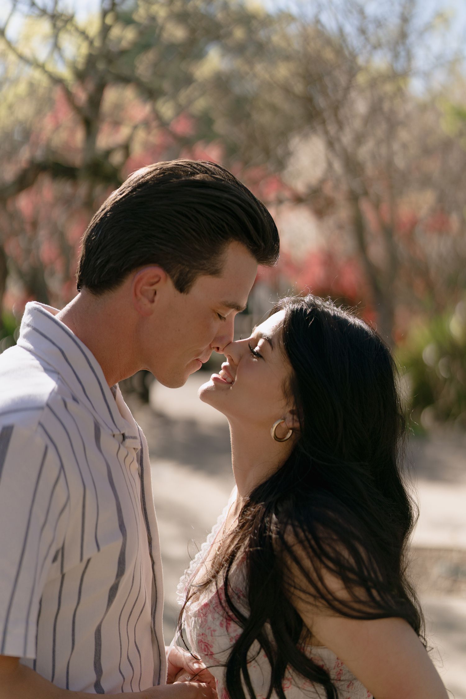 Romantic couple sharing an intimate moment outdoors, surrounded by blooming pink flowers in soft natural light.