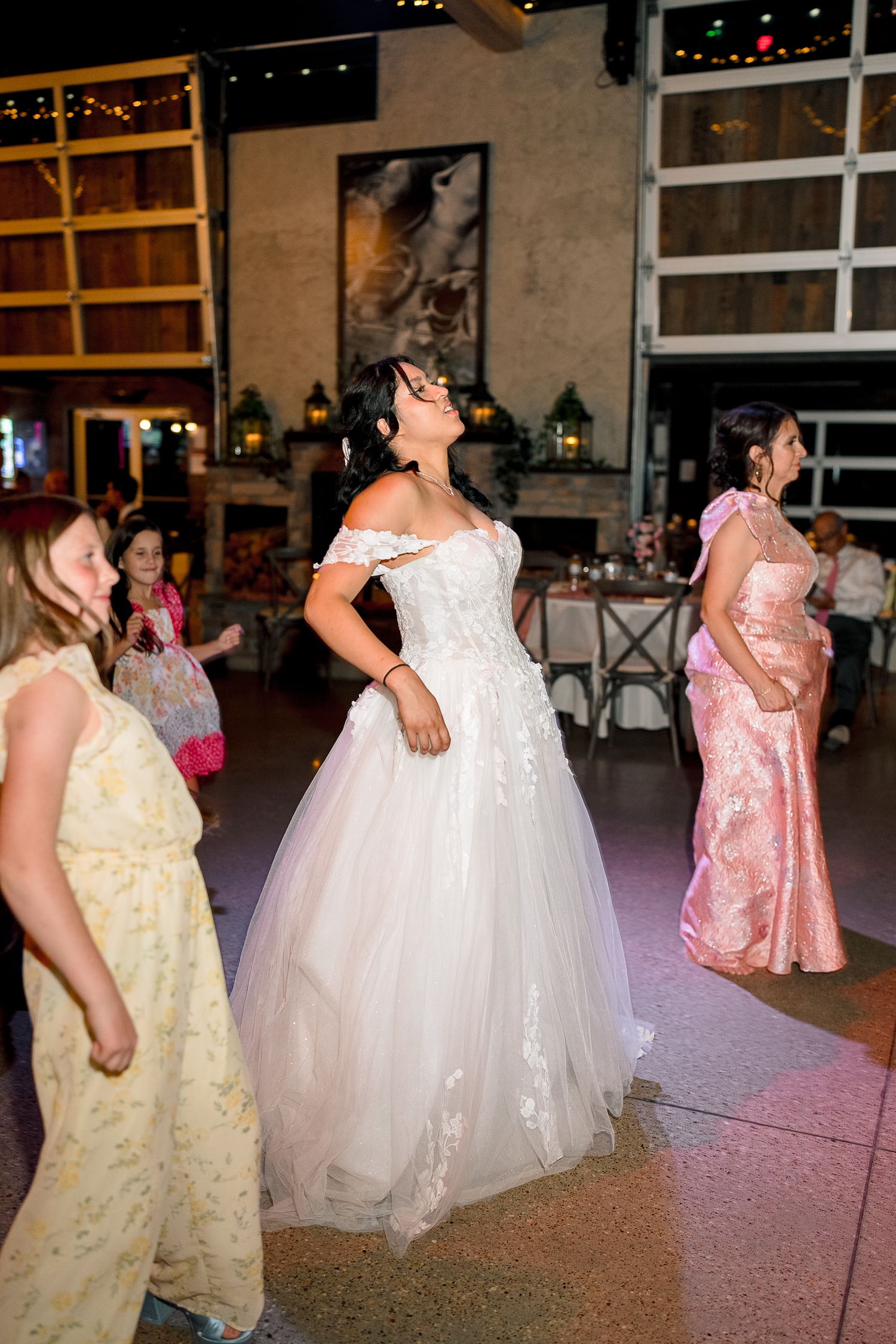 Bride dances joyfully on the reception dance floor in her off-shoulder lace ball gown wedding dress.