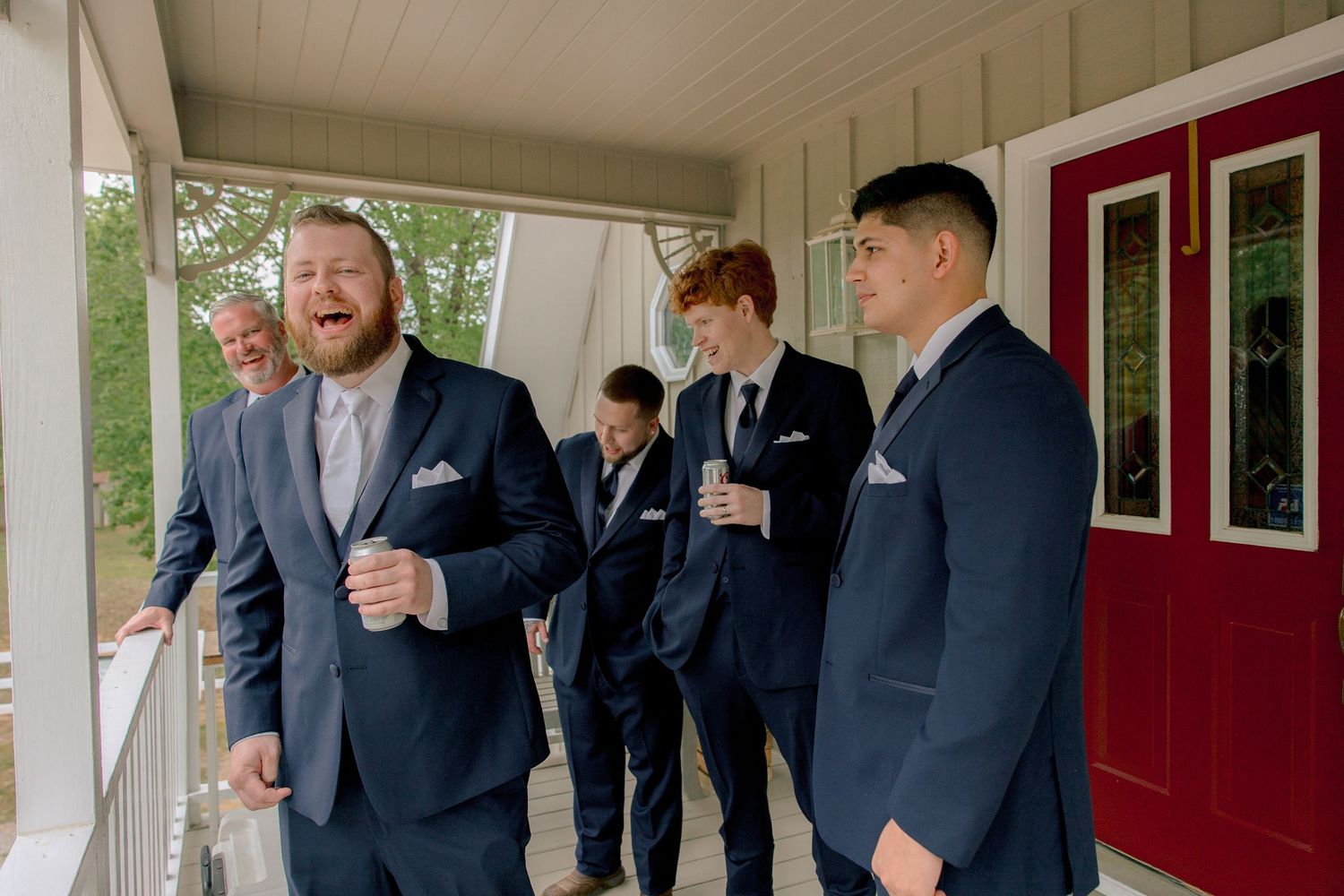 Groomsmen in navy suits laughing on porch before wedding ceremony.
