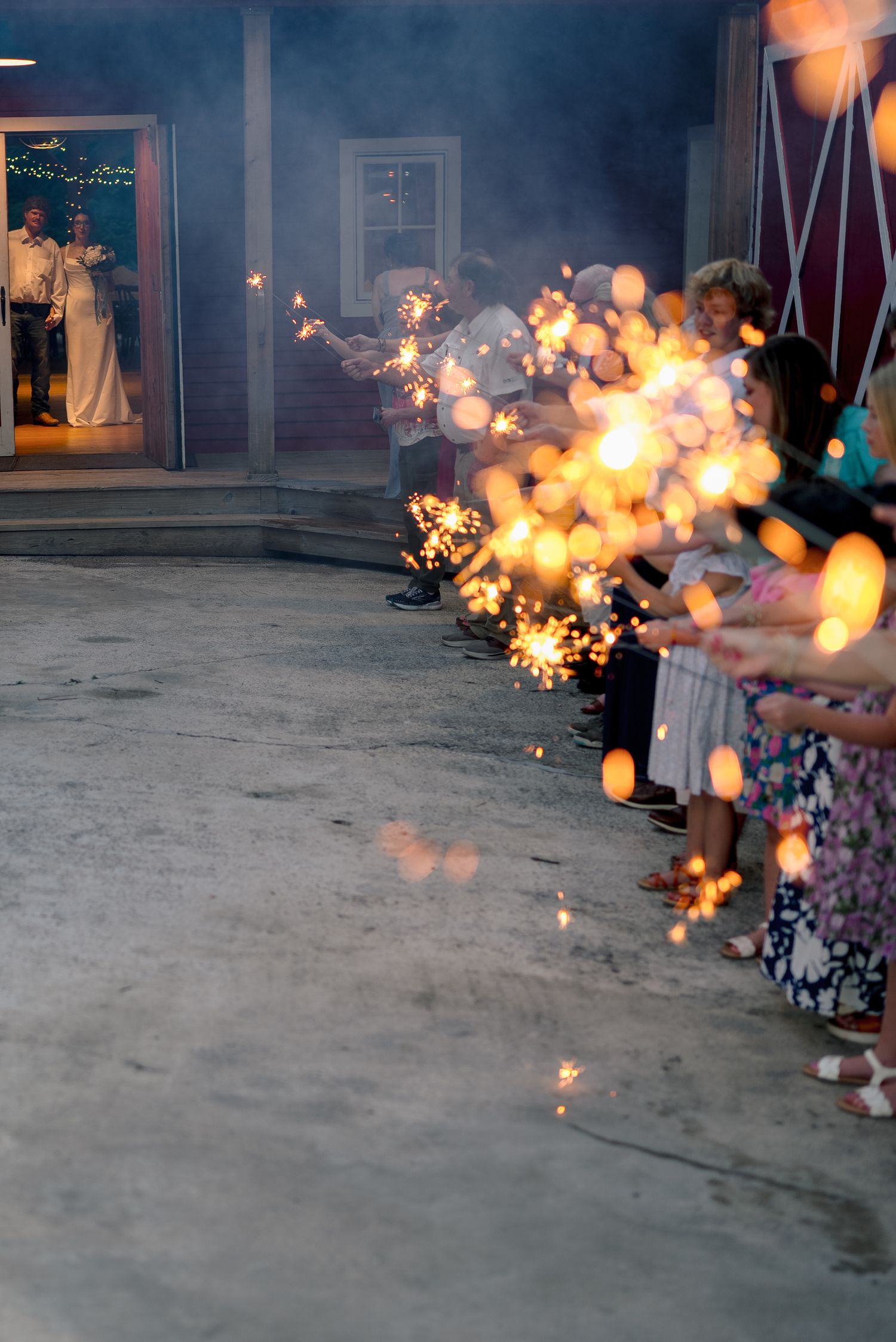 Wedding guests line up holding sparklers to create a glowing exit tunnel for the newlyweds at an evening celebration.