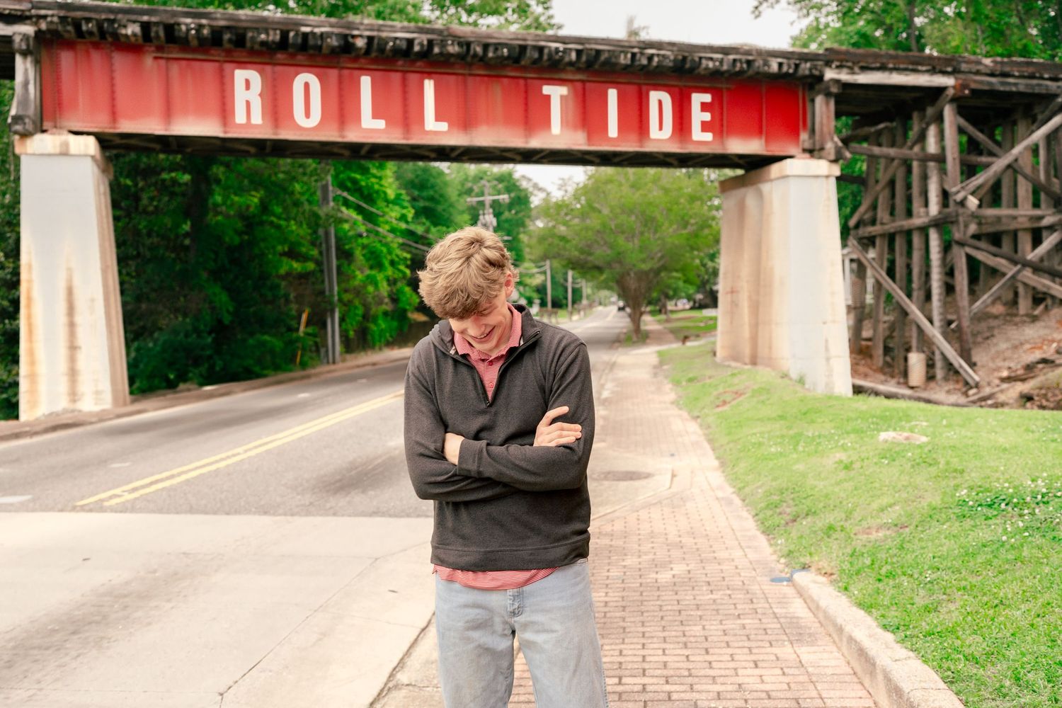 A student stands with crossed arms under the historic Roll Tide bridge.