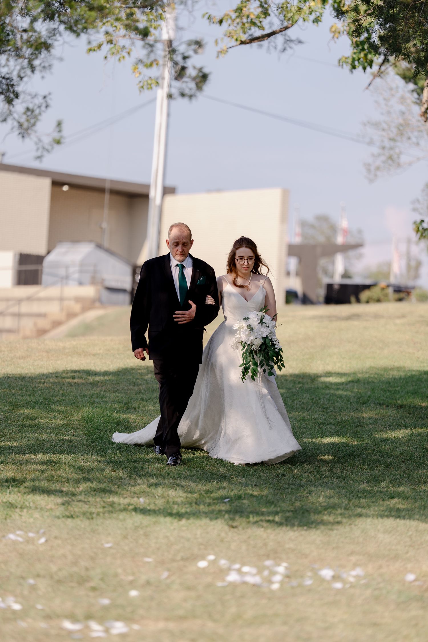 A couple walks arm in arm across a grassy lawn during an outdoor wedding ceremony.