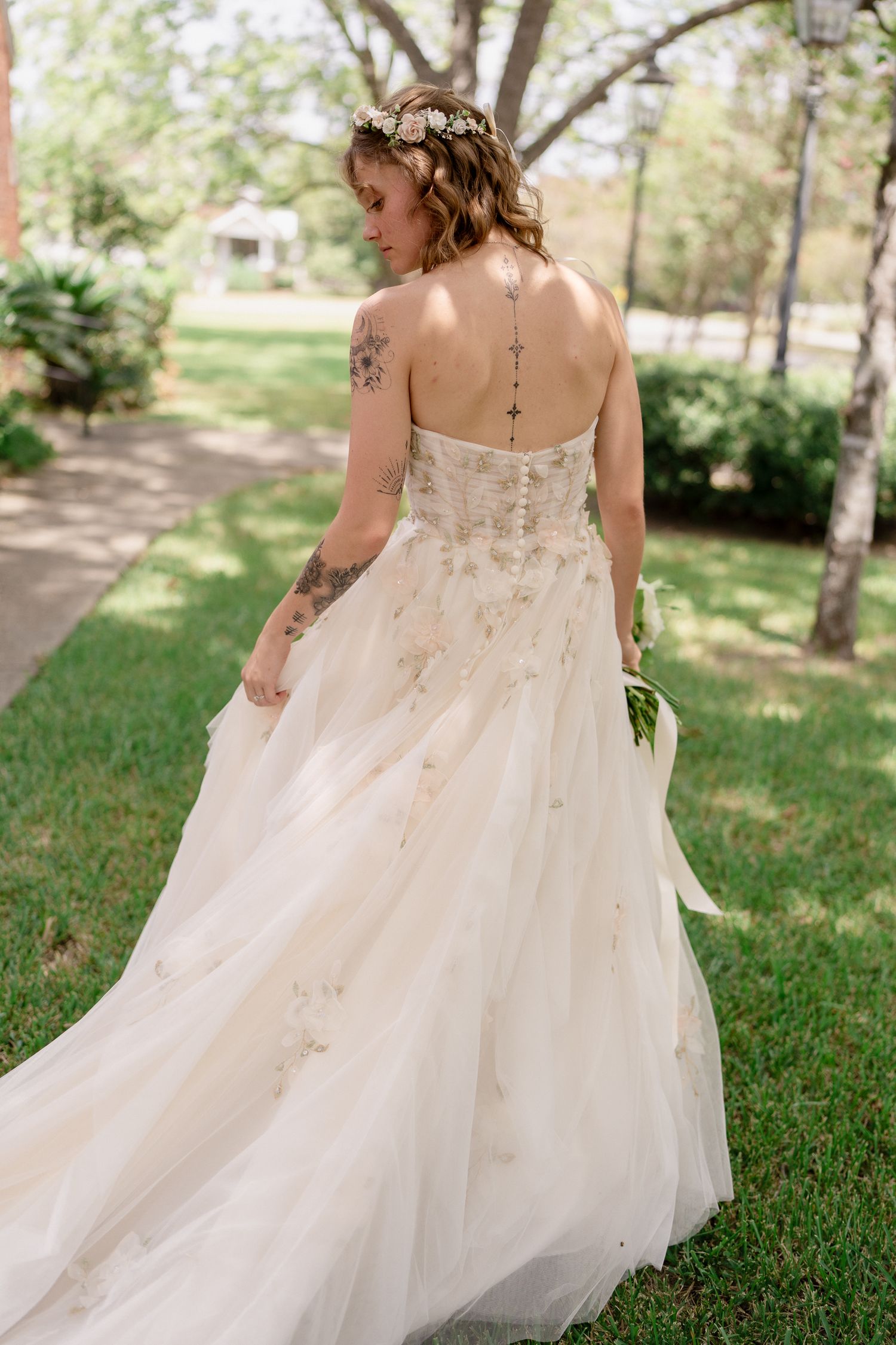 A flowing white wedding dress with delicate details and lace back is captured in motion outdoors.