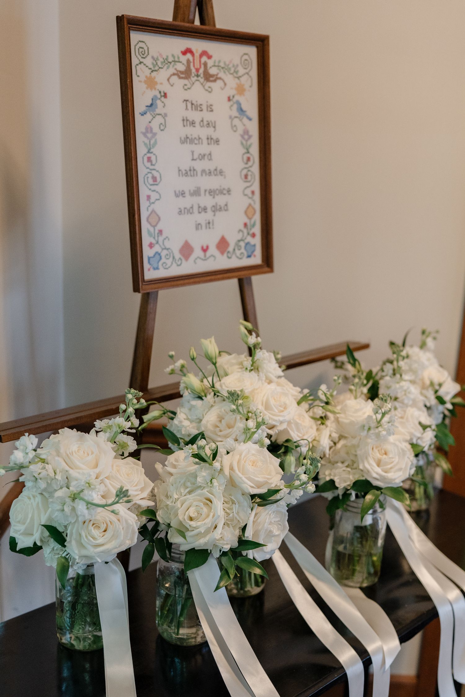 White roses and floral arrangements in mason jars with white ribbons displayed beneath framed wall art.