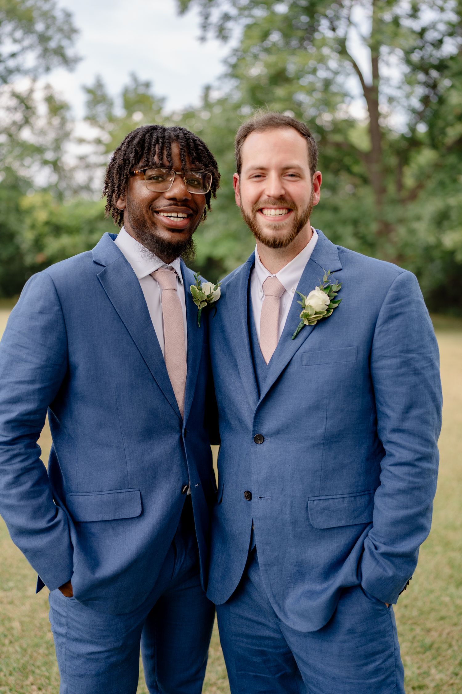Groomsmen in coordinated navy suits and blush pink ties pose together on a grassy lawn.