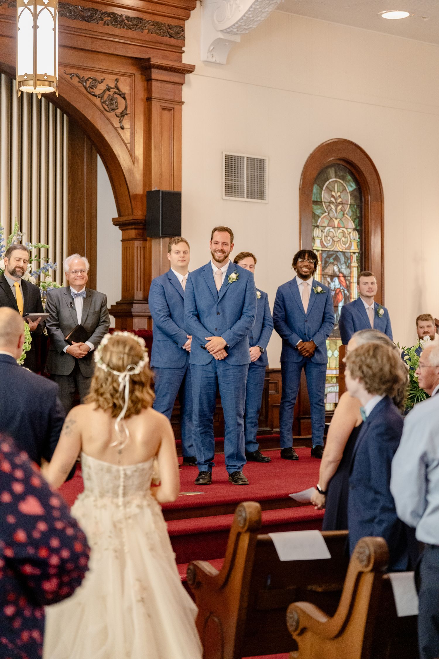 Wedding party stands in a line at the altar inside an elegant church with wooden architectural details.