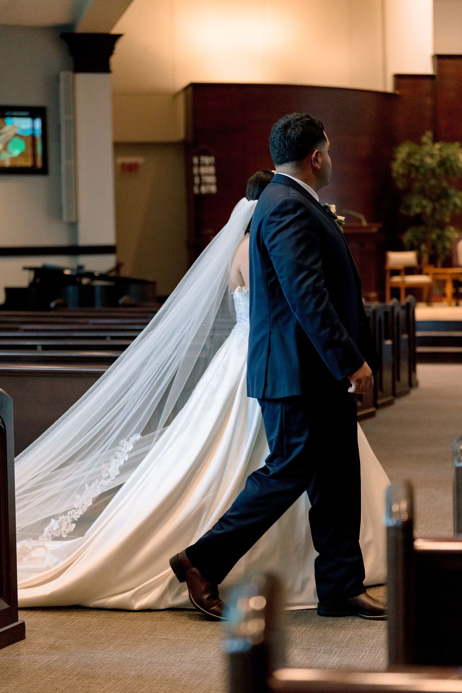 A wedding couple's silhouette in a church aisle with a flowing white bridal train trailing behind them.