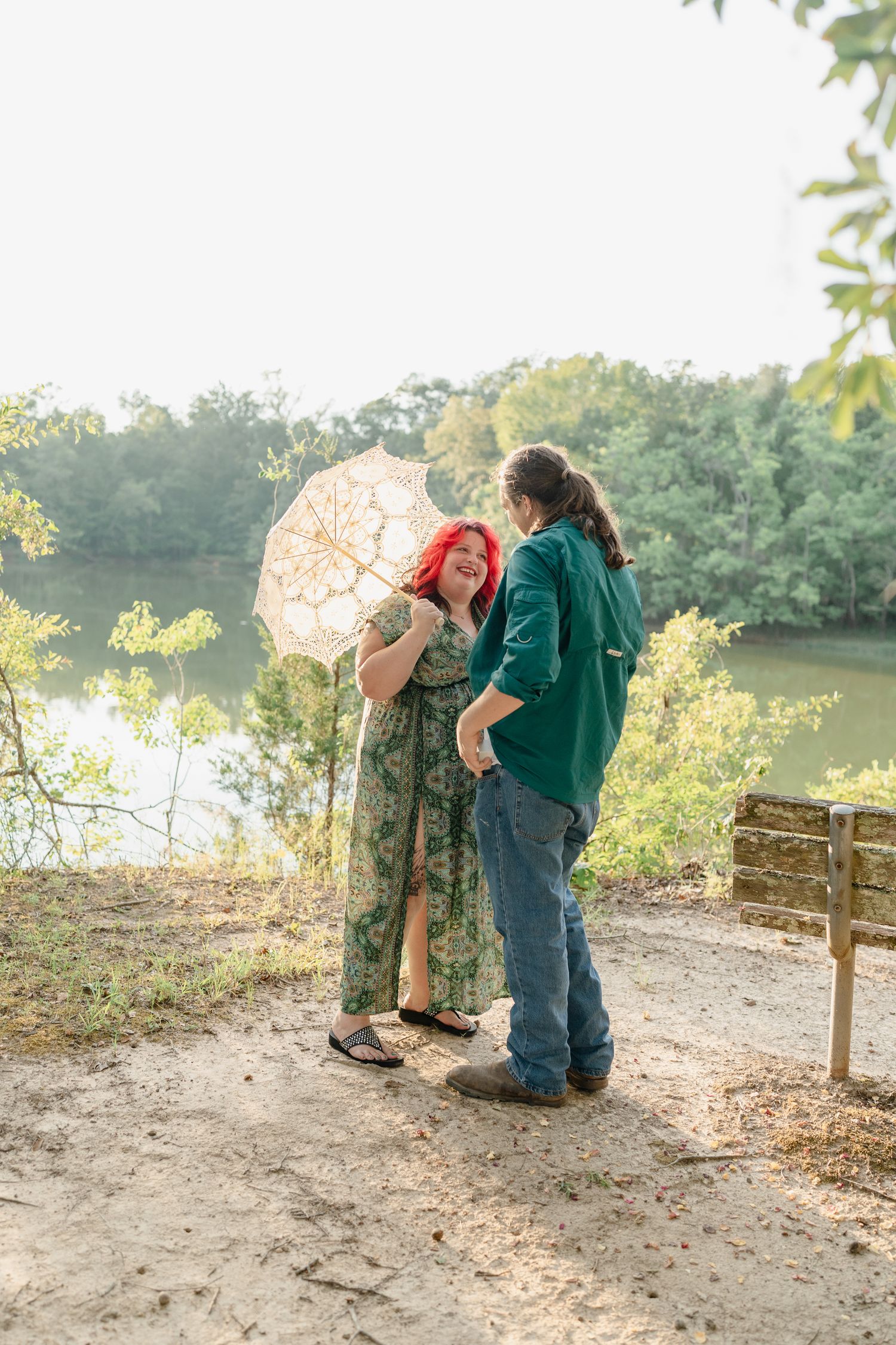 A couple poses together on a scenic trail with a white lace parasol during sunset.