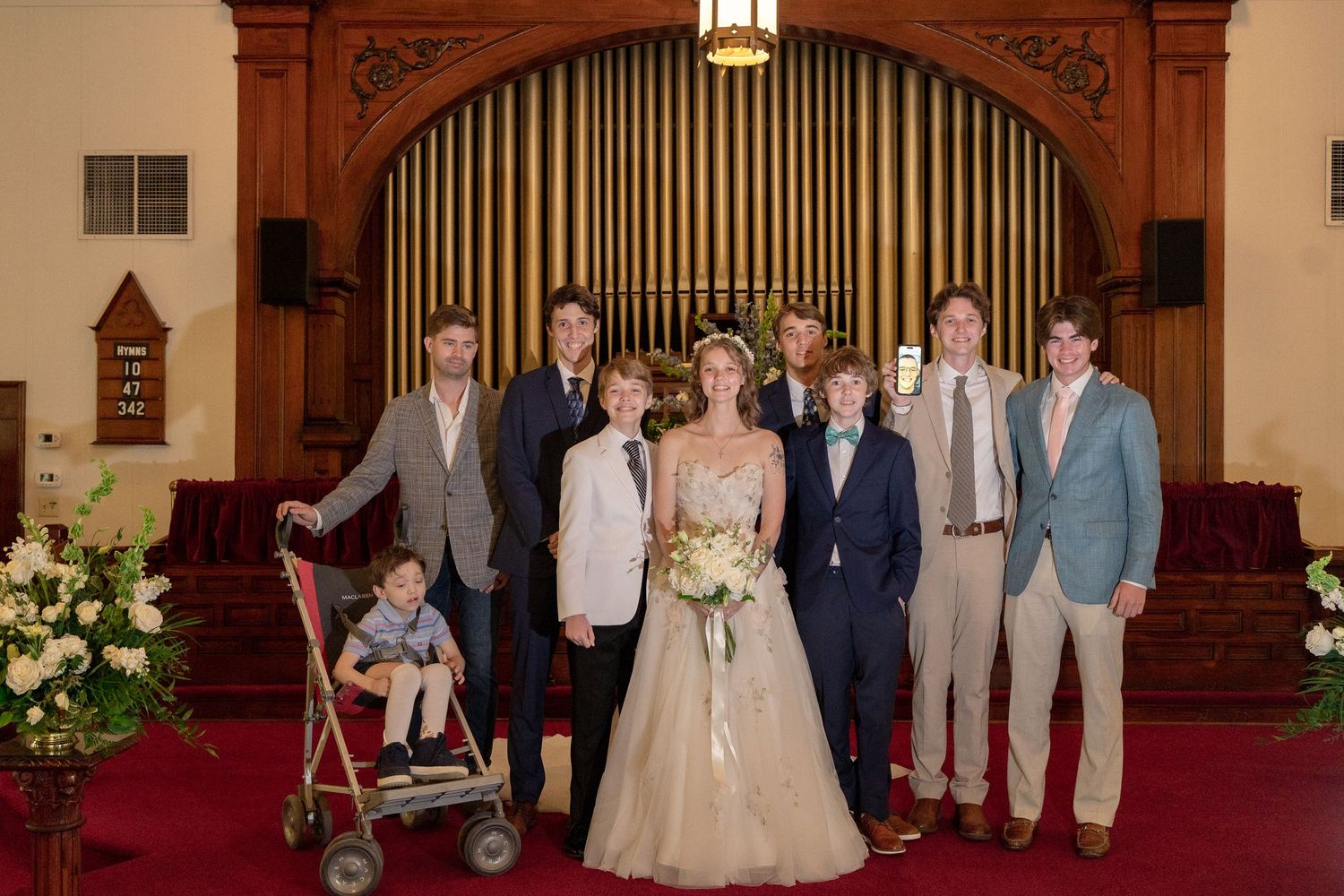 Wedding party members pose together in a formal church setting with ornate wooden decor and stained glass windows.
