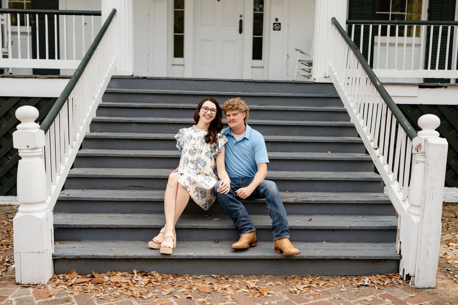 A couple shares a relaxed moment sitting on outdoor stairs of a white building.