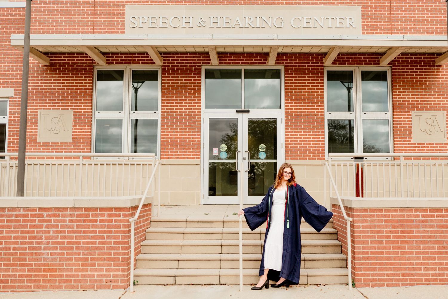 Graduate celebrates with dramatic poses on stairs outside brick learning center.