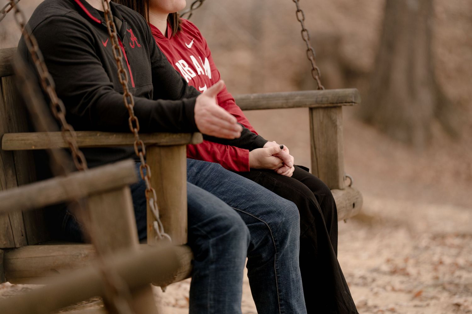 A person in a red sweater and jeans sits on a wooden fence in an autumn forest setting.