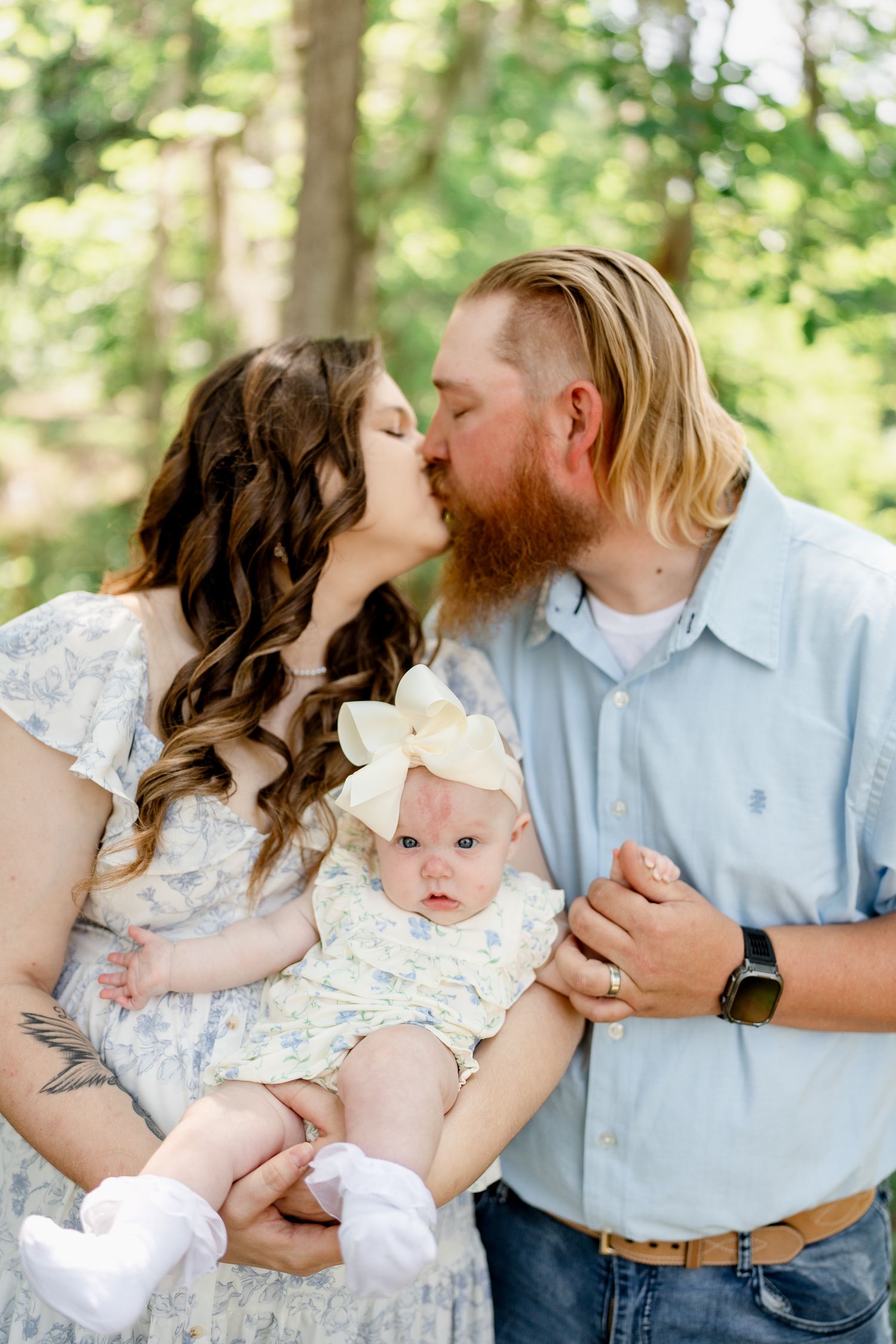 Sweet family moments captured in sunlit forest with baby in floral outfit.