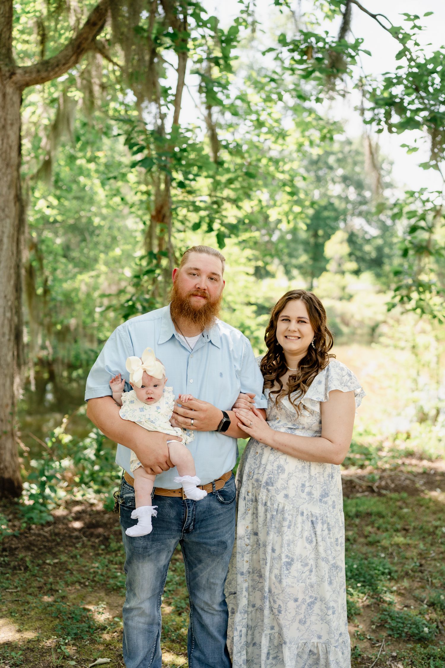 A family poses together in a wooded setting wearing coordinated blue and white outfits.