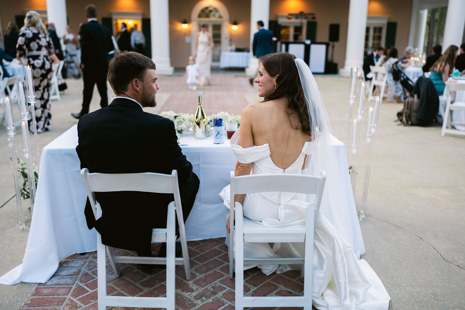 A couple sits at an elegant wedding reception table with white linens and decor.