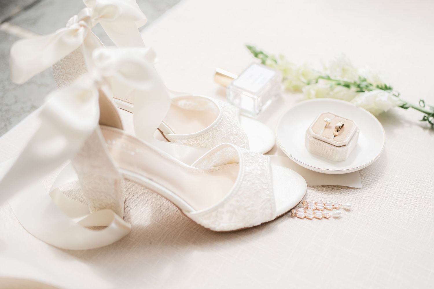 White delicate wedding shoes arranged with floral elements on light background.
