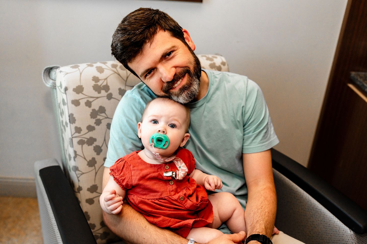 Tender family moments with a baby and caregiver on a patterned chair.