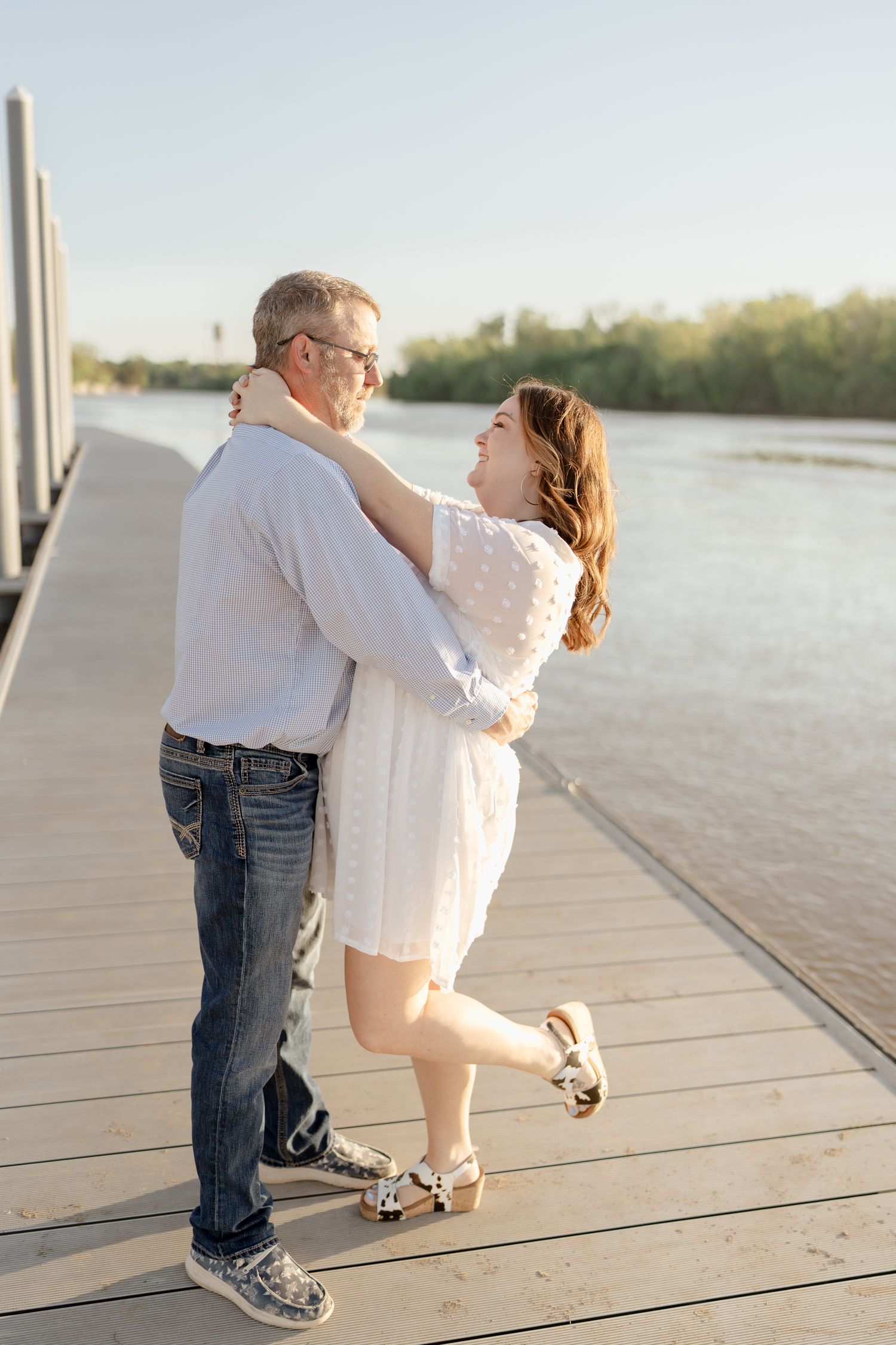 A couple dances together on a wooden boardwalk overlooking the water.