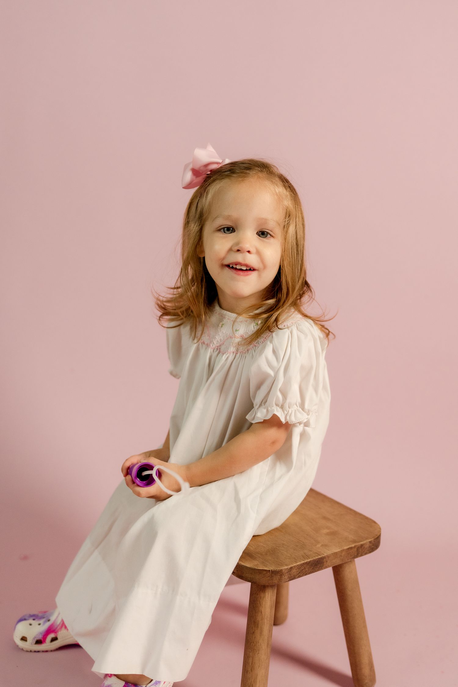 A cheerful scene with a small child in a white dress sitting on a wooden stool.