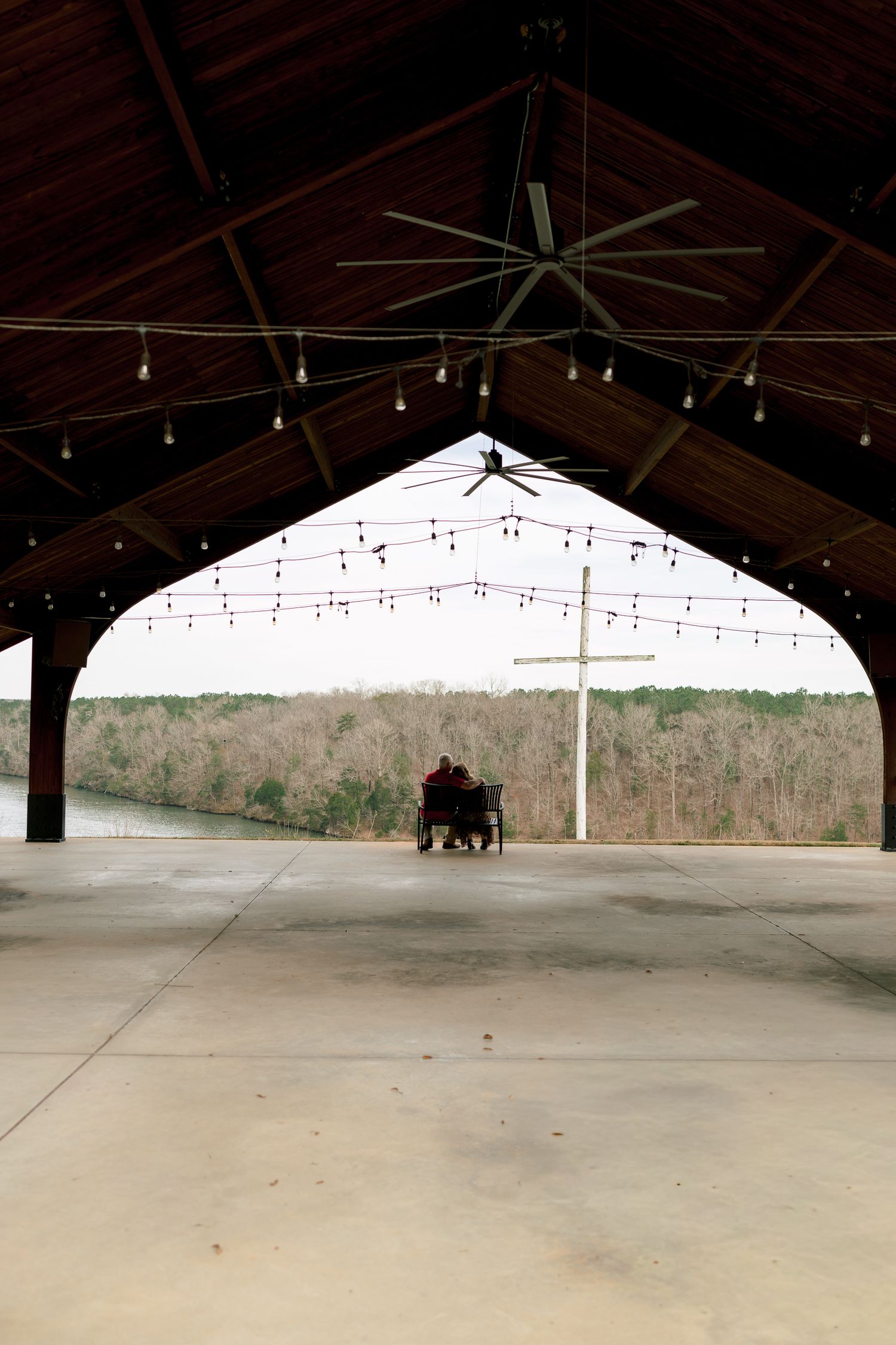 Couple sits together in a rustic open-air venue with string lights and a cross outside.