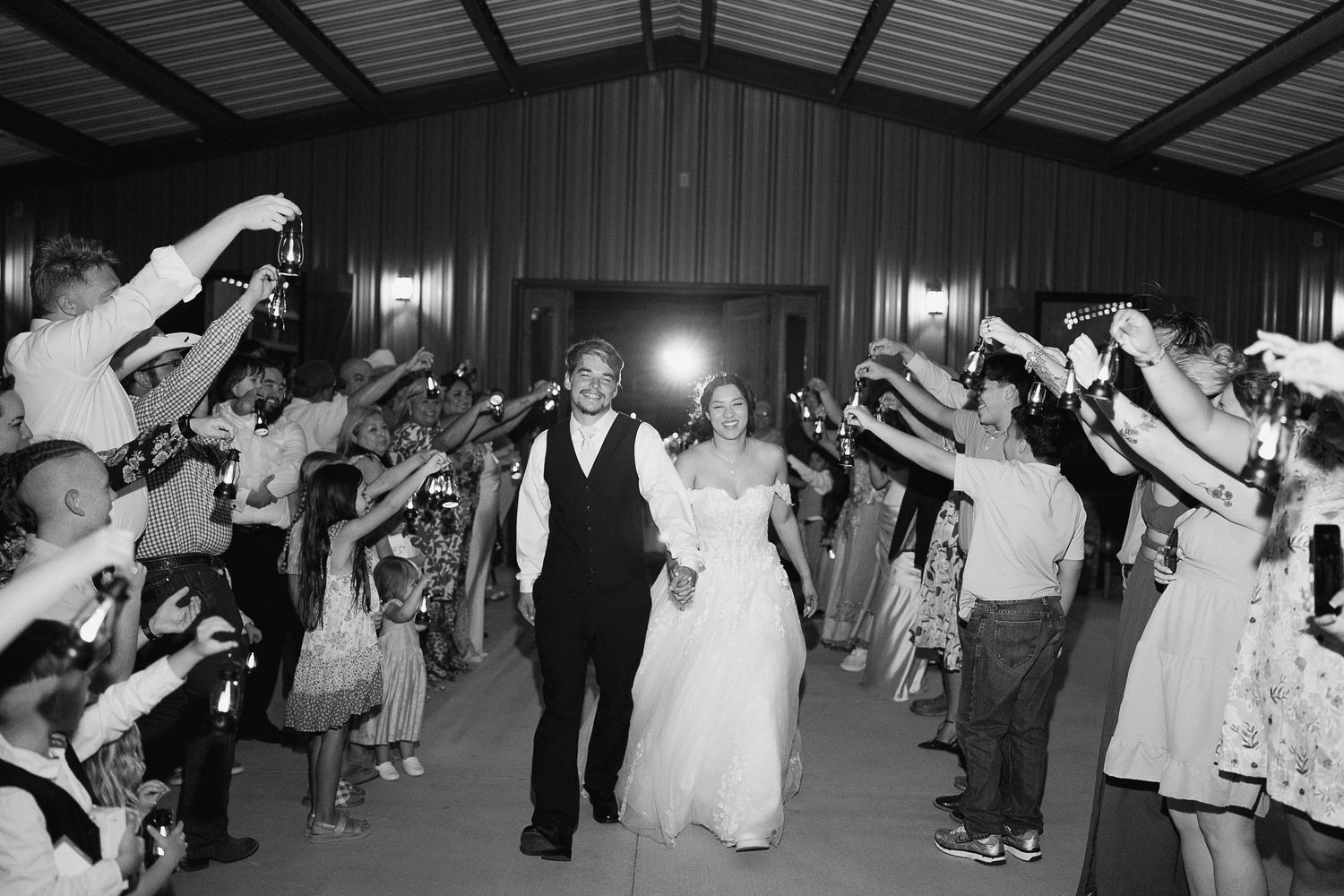Newlyweds exit reception hall through sparkler tunnel surrounded by cheering wedding guests.