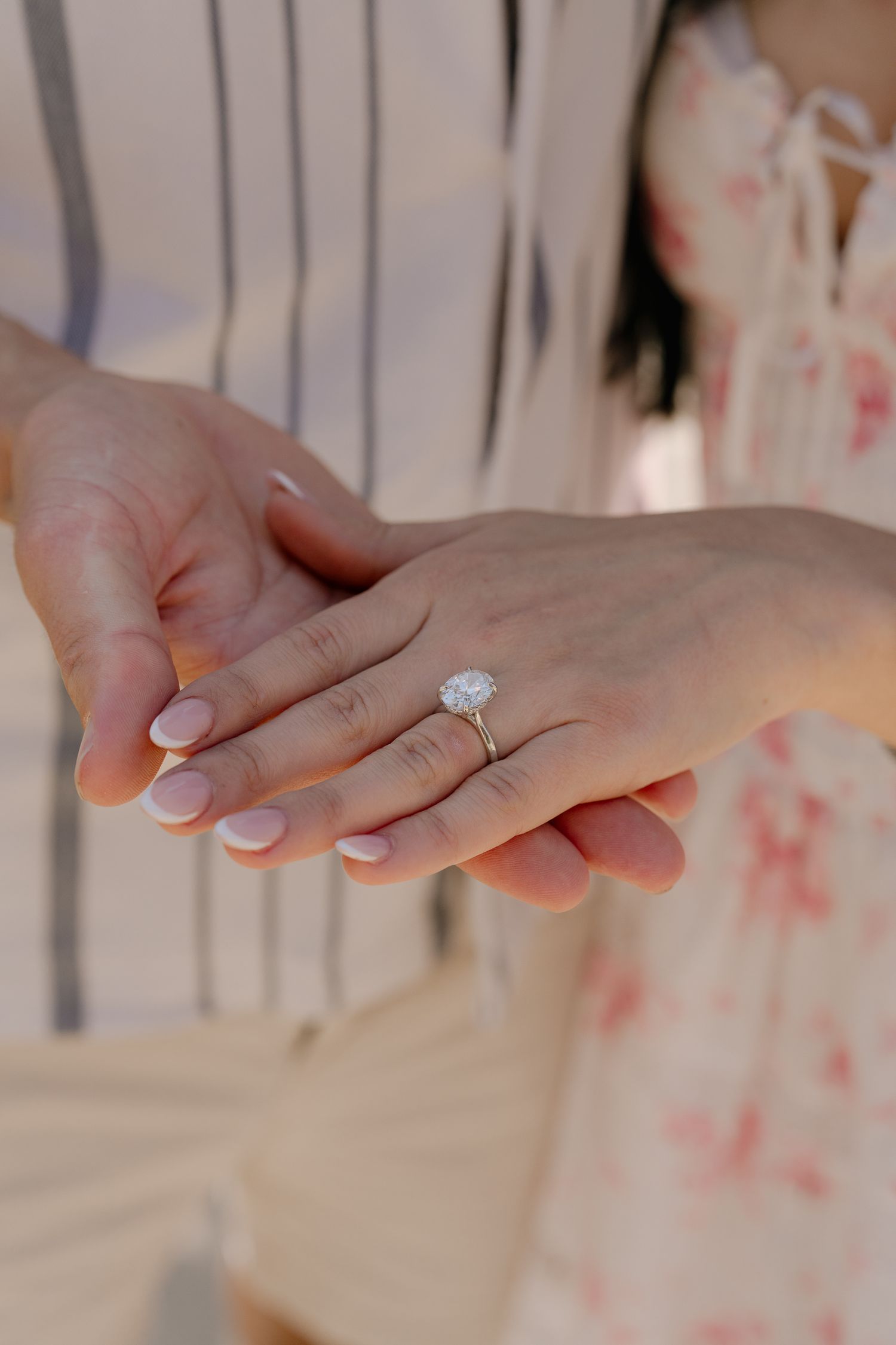 Close-up of hands displaying a stunning oval diamond solitaire engagement ring on ring finger with nude manicure.