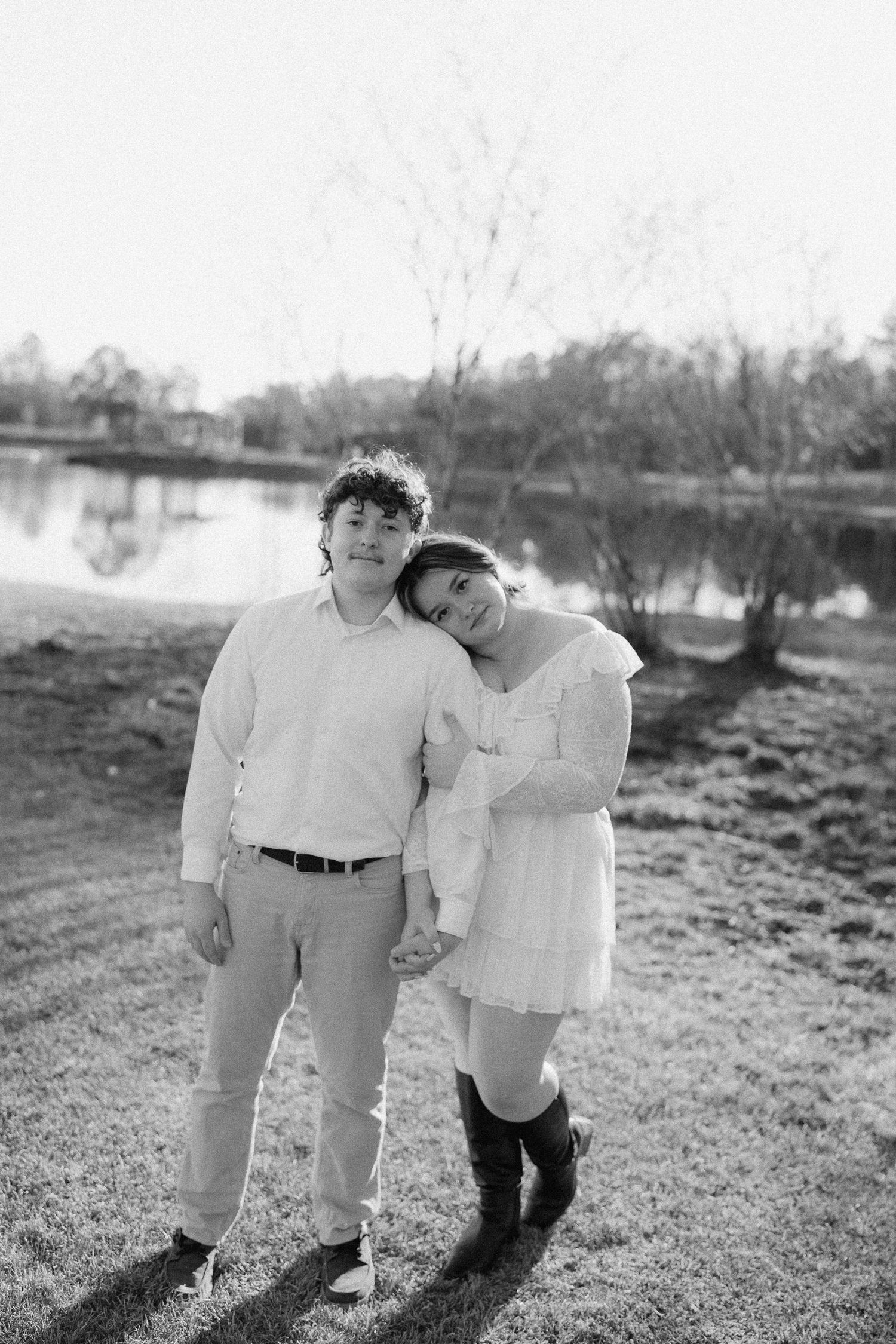 Black and white portrait of couple standing close together holding hands near a tranquil lake.