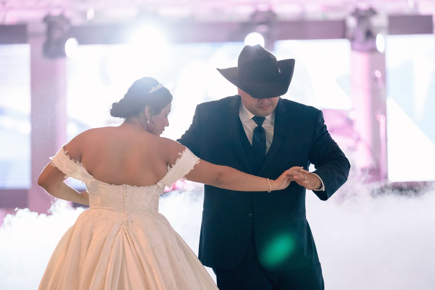 Couples dancing together at a wedding reception in a bright white venue with soft pink lighting.