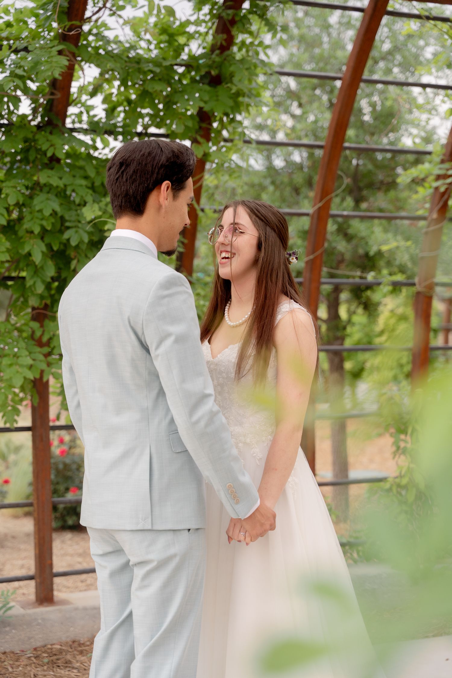 A couple shares a romantic moment under a rustic wooden pergola surrounded by green foliage.
