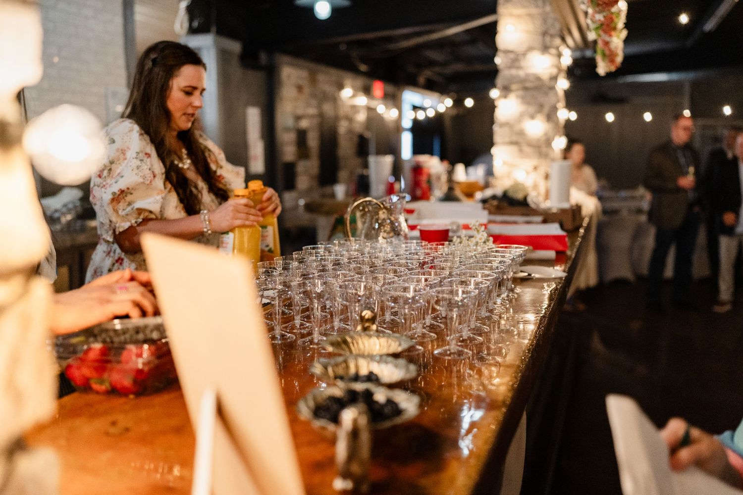 Bartender pouring multiple cocktails simultaneously at a dimly lit bar counter with glassware lined up.