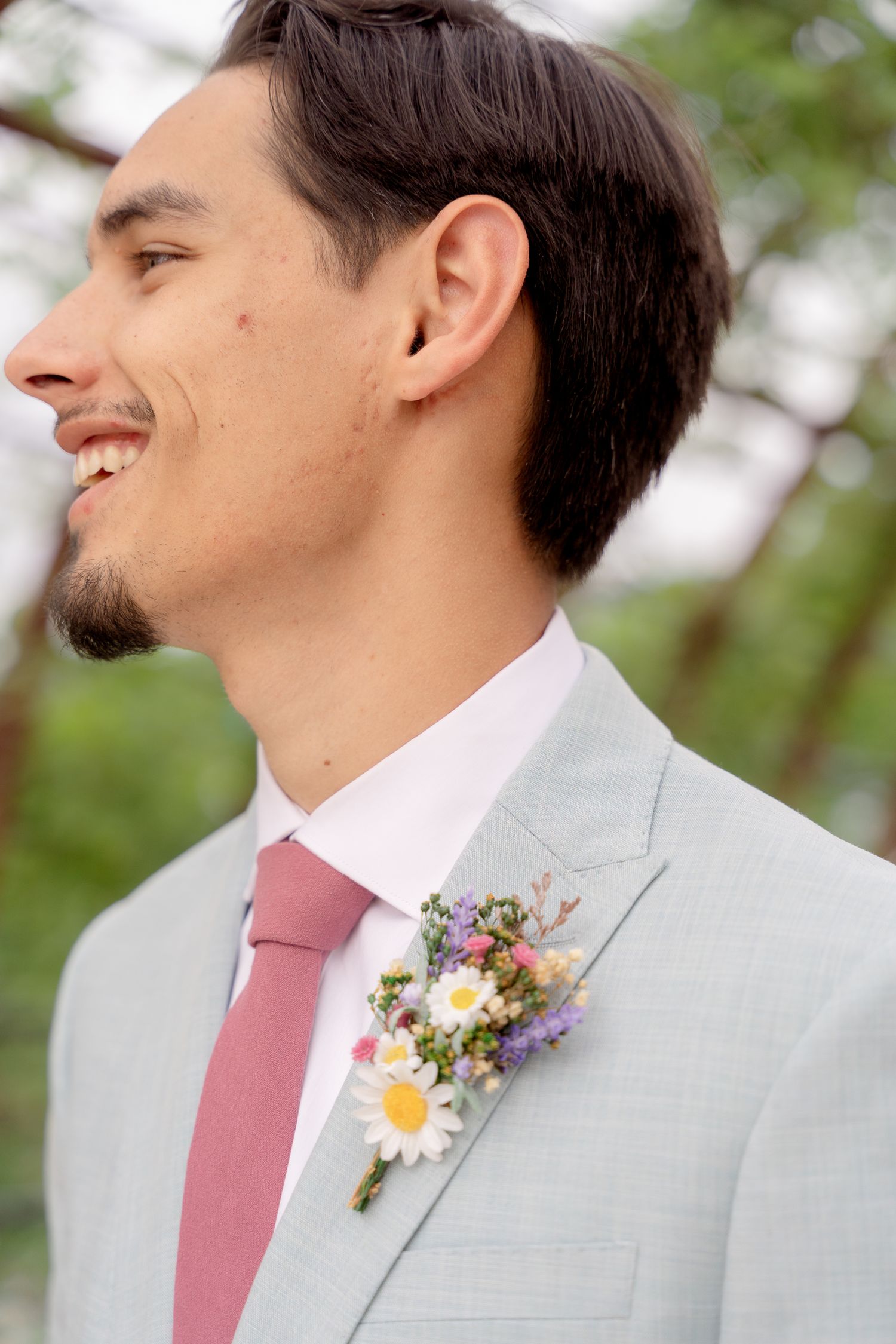 A close-up view of a boutonniere with pink and purple wildflowers pinned to a light gray suit jacket.