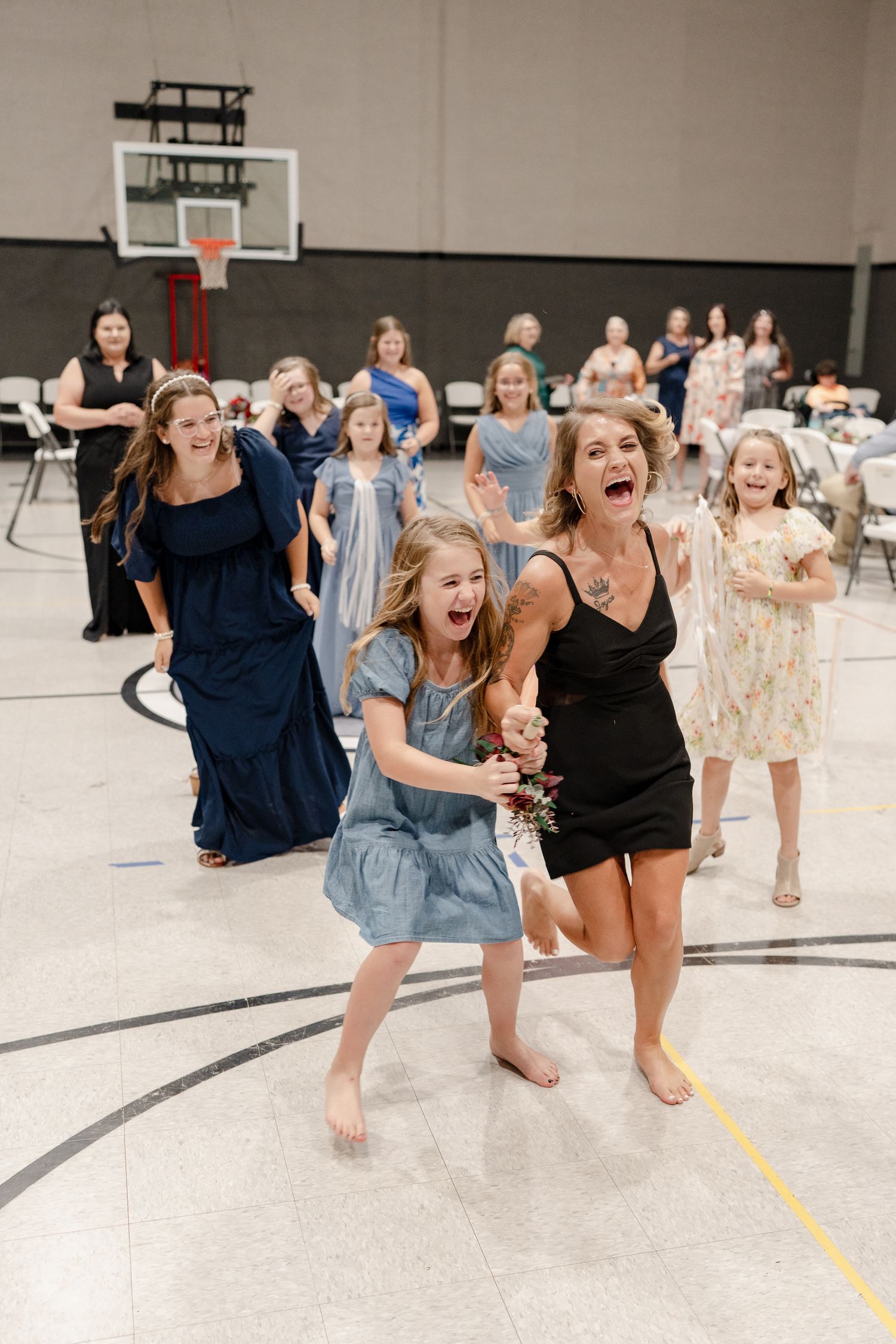 A group of people dancing and jumping with joy on a gymnasium floor at a celebration event.