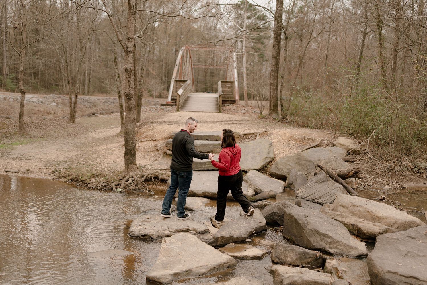 A couple explores rocky terrain near a stream in a natural outdoor setting.