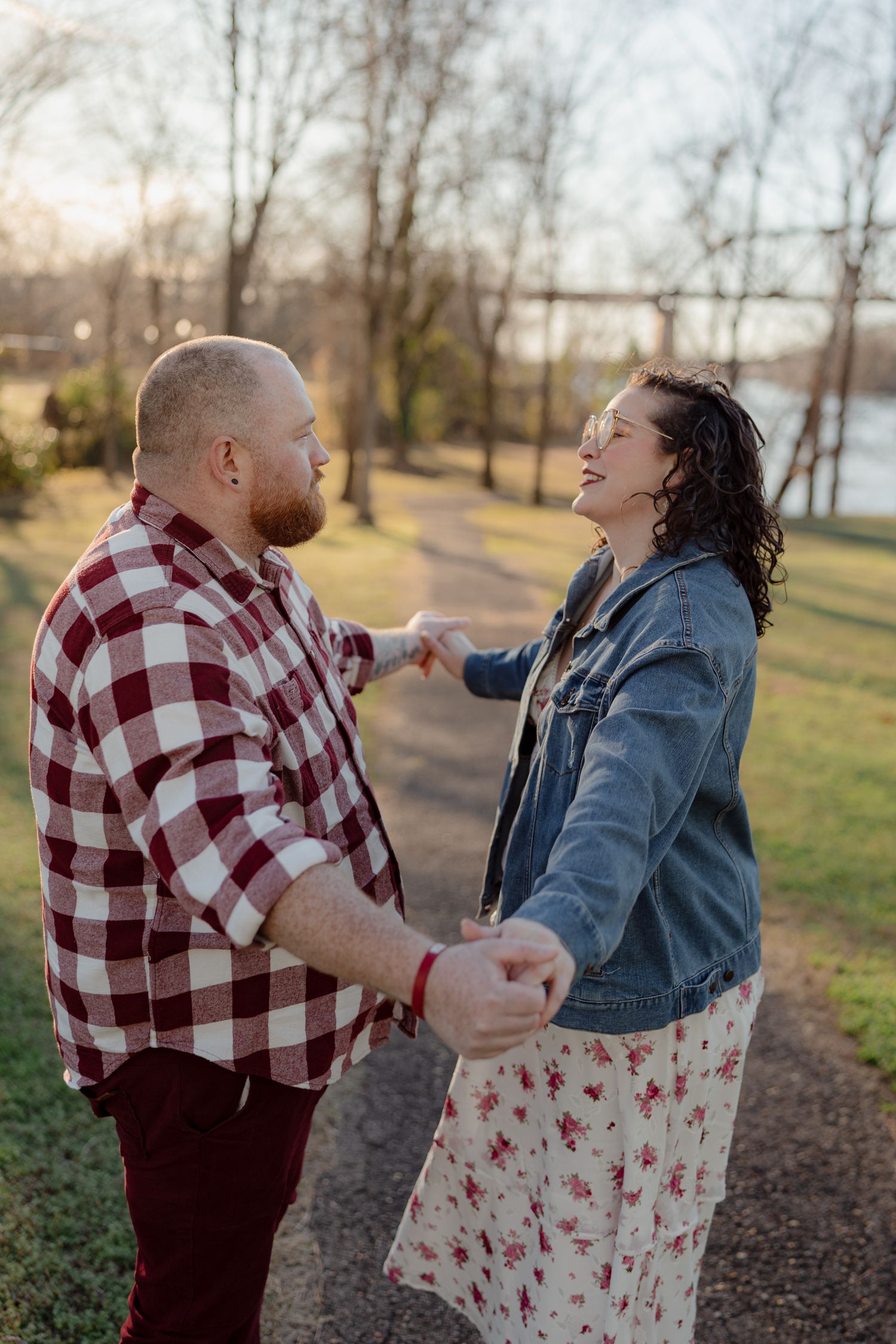 A couple dances and laughs together on a path in a park during sunset.